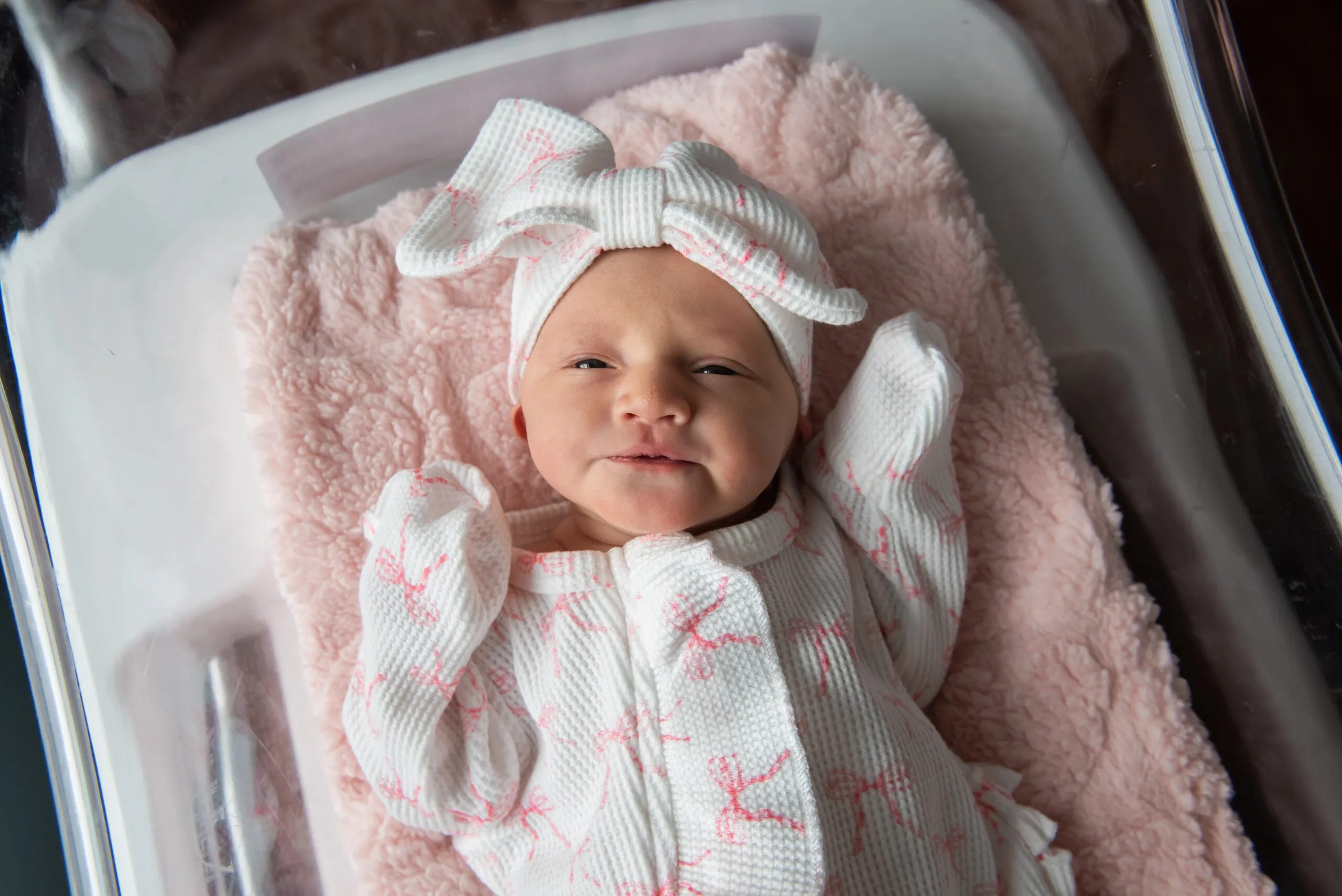 Newborn baby in white jumpsuit laying down and staring at camera.