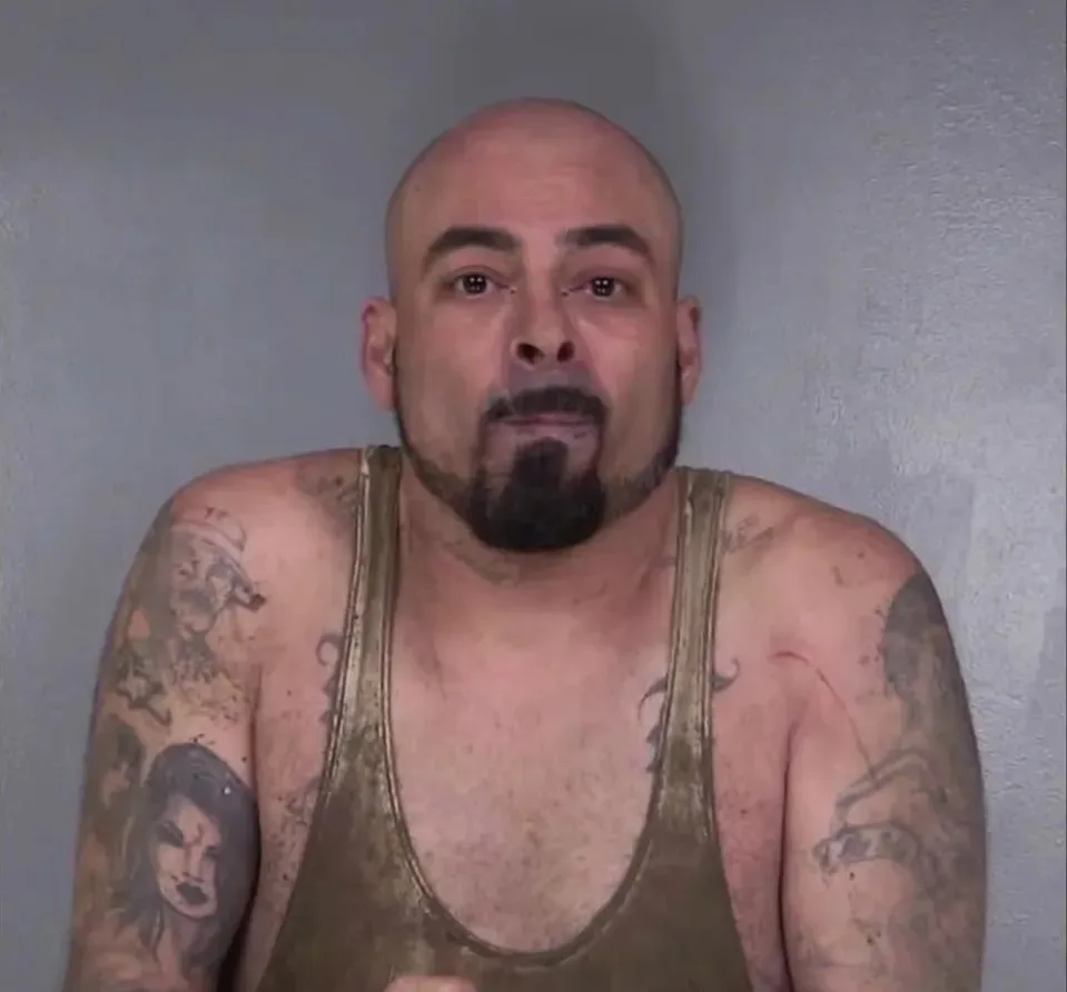 Man wearing brown singlet with tattoos staring at camera.
