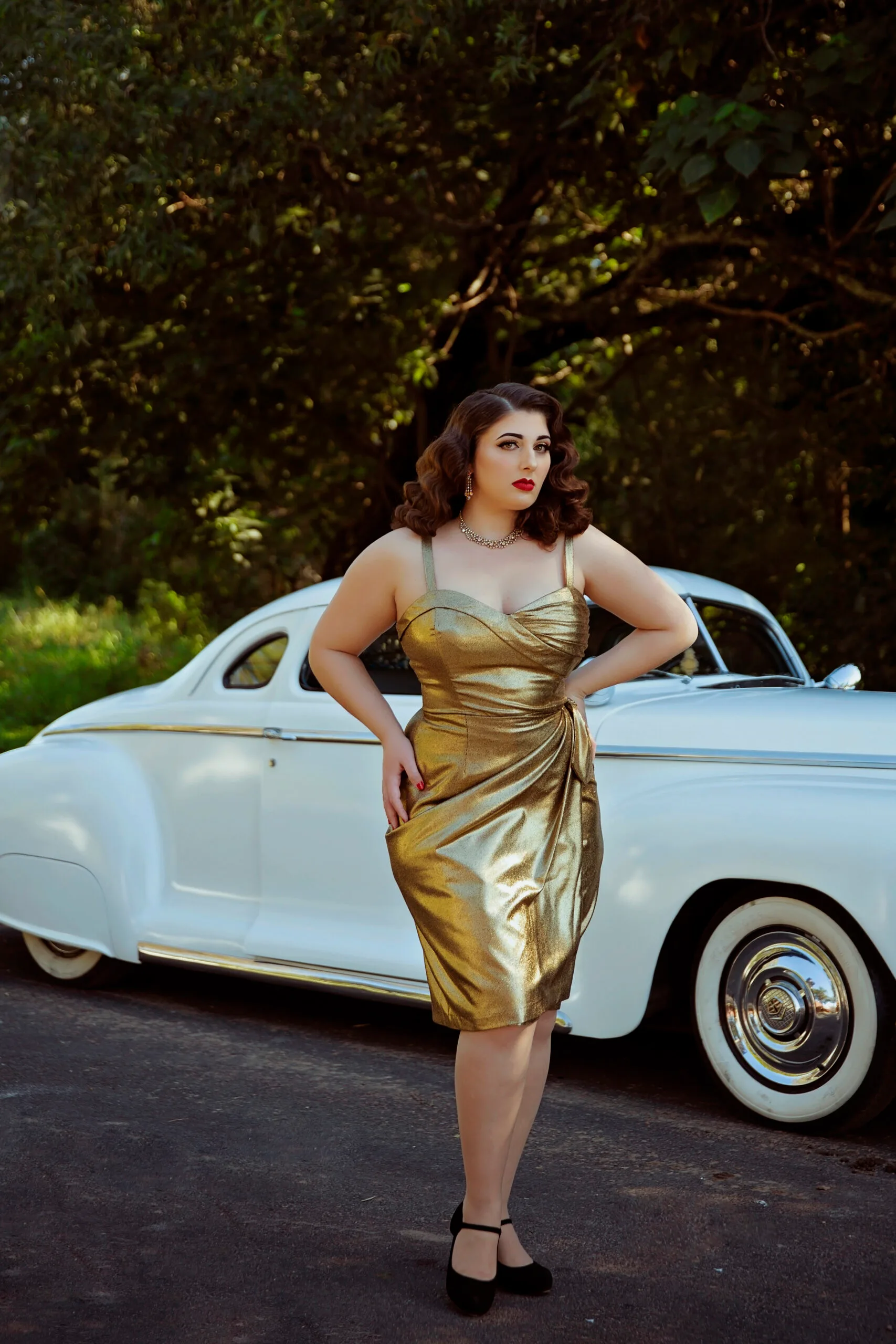 Woman wearing long golden sparkly dress, posing infront of blue vintage car.