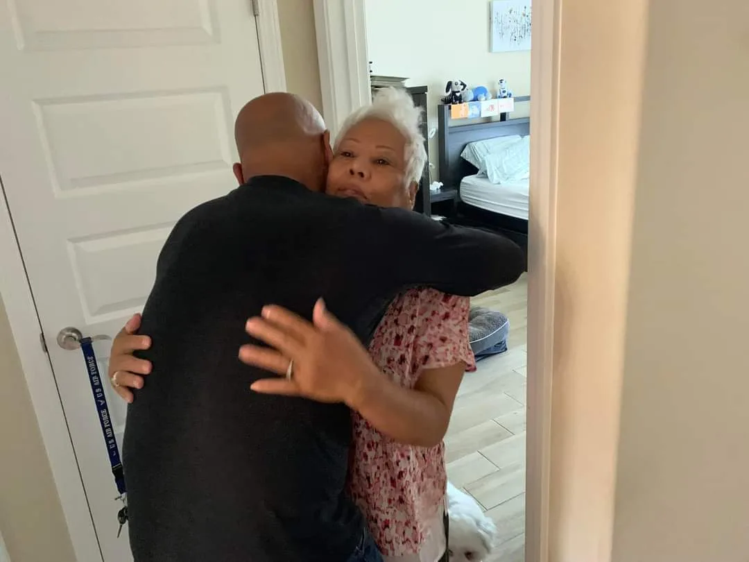 Man hugging elderly woman, wearing floral top. 