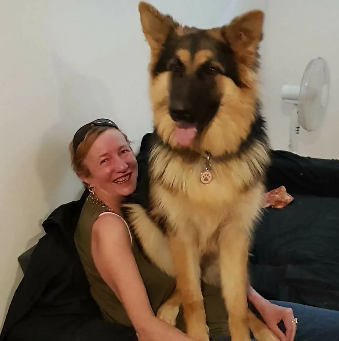 Woman wearing green top sitting on couch with large dog sitting on her lap.