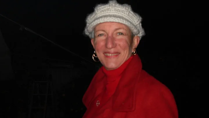 Woman wearing red coat over red turtleneck and white beanie, looking at camera and smilling. 