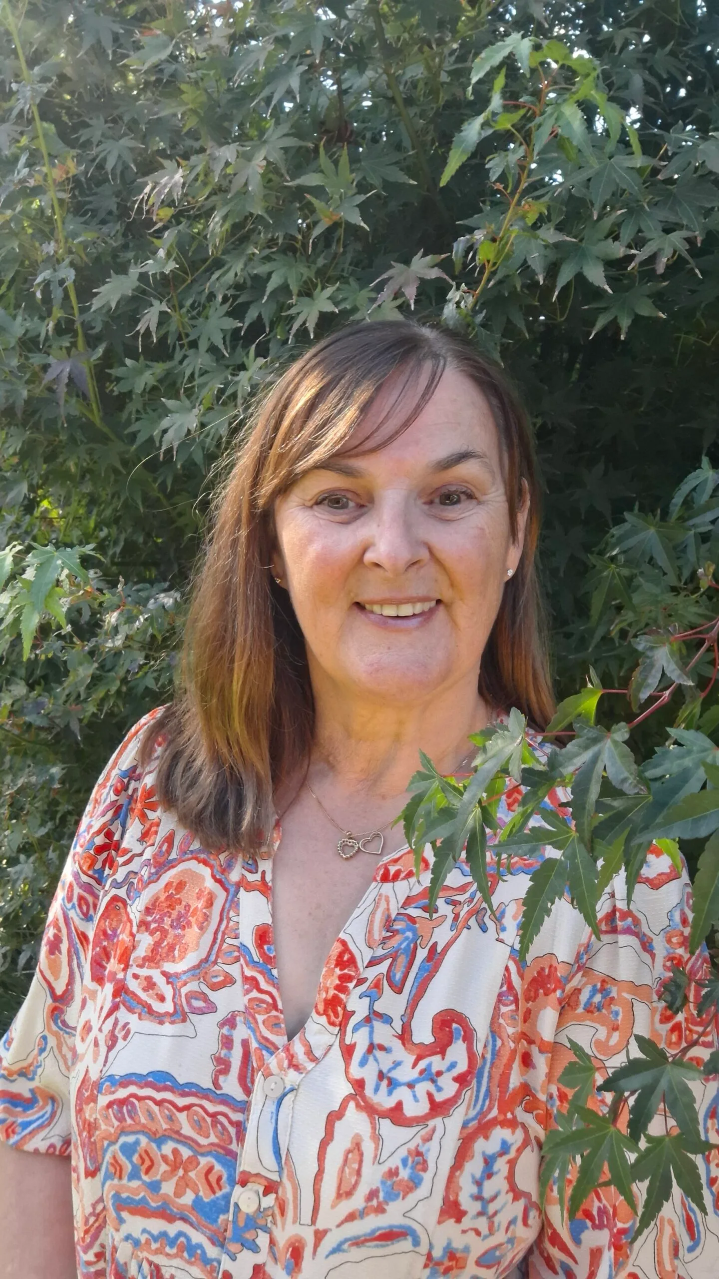 Tracey standing in colourful shirt by a tree