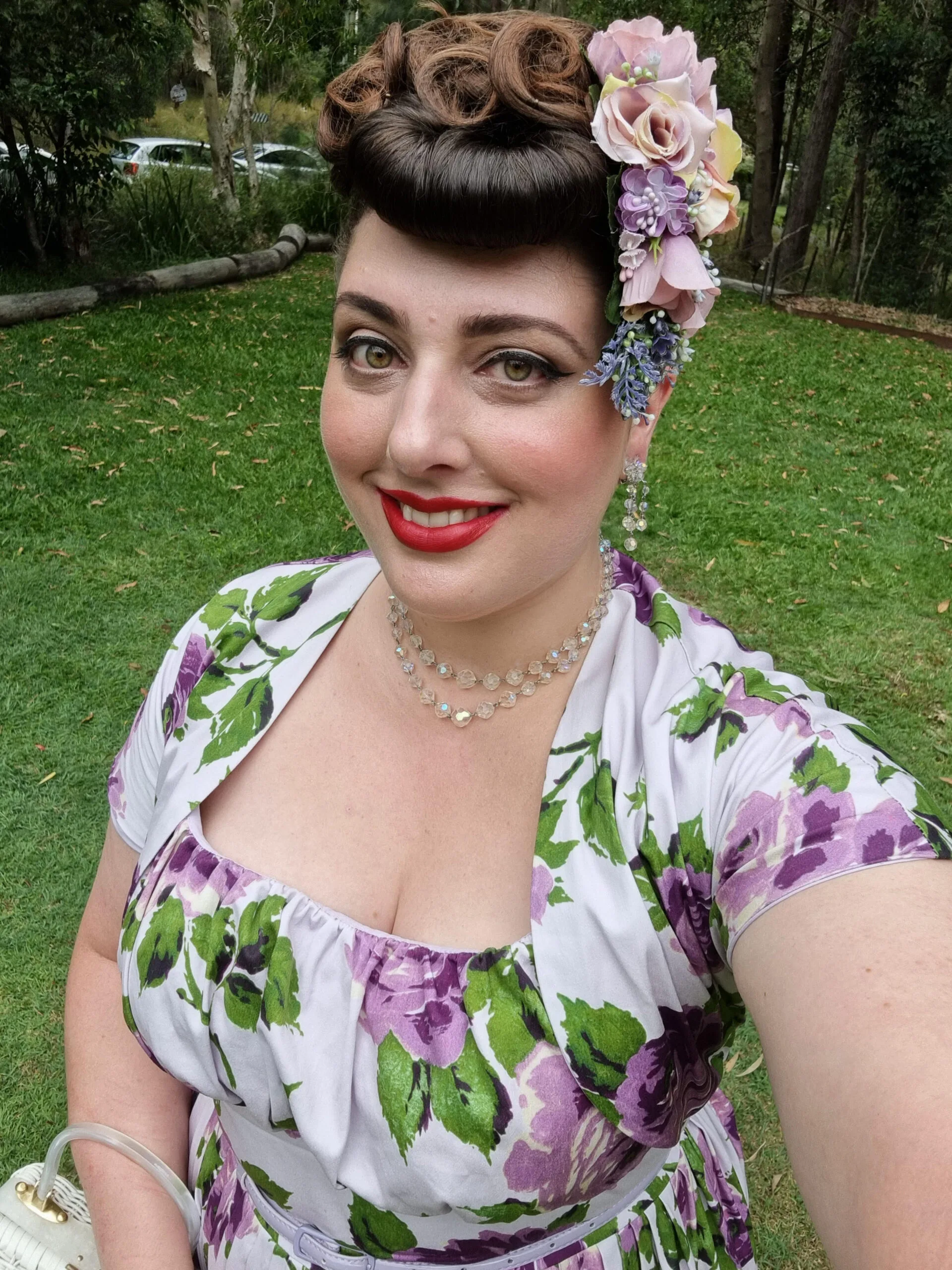 Woman with a pin up bun and flower accessories in her hair, wearing floral vintage dress and smilling at camera. 