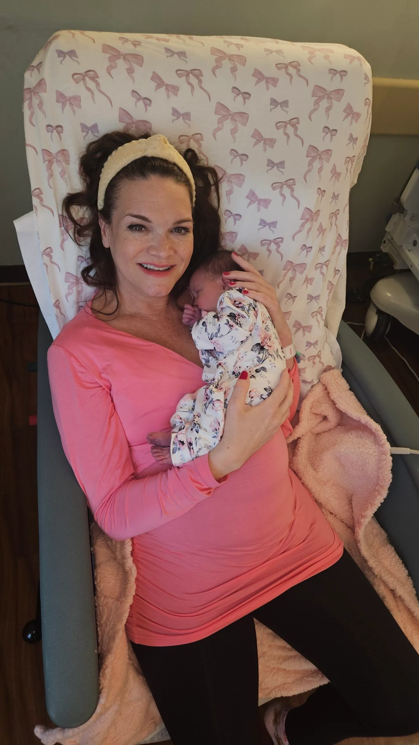 Woman wearing pink long top holding newborn baby on chest, sitting on a couch.