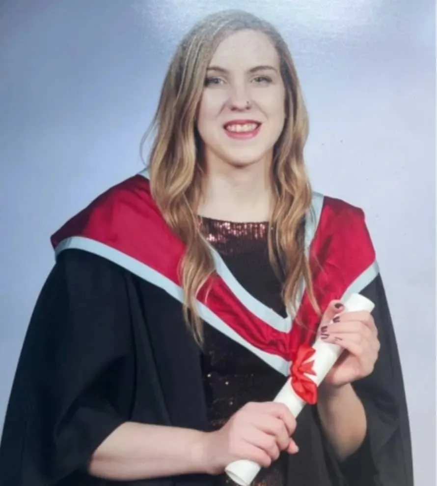 Woman with blonde hair wearing graduation cape and holding certificate and smilling at camera.