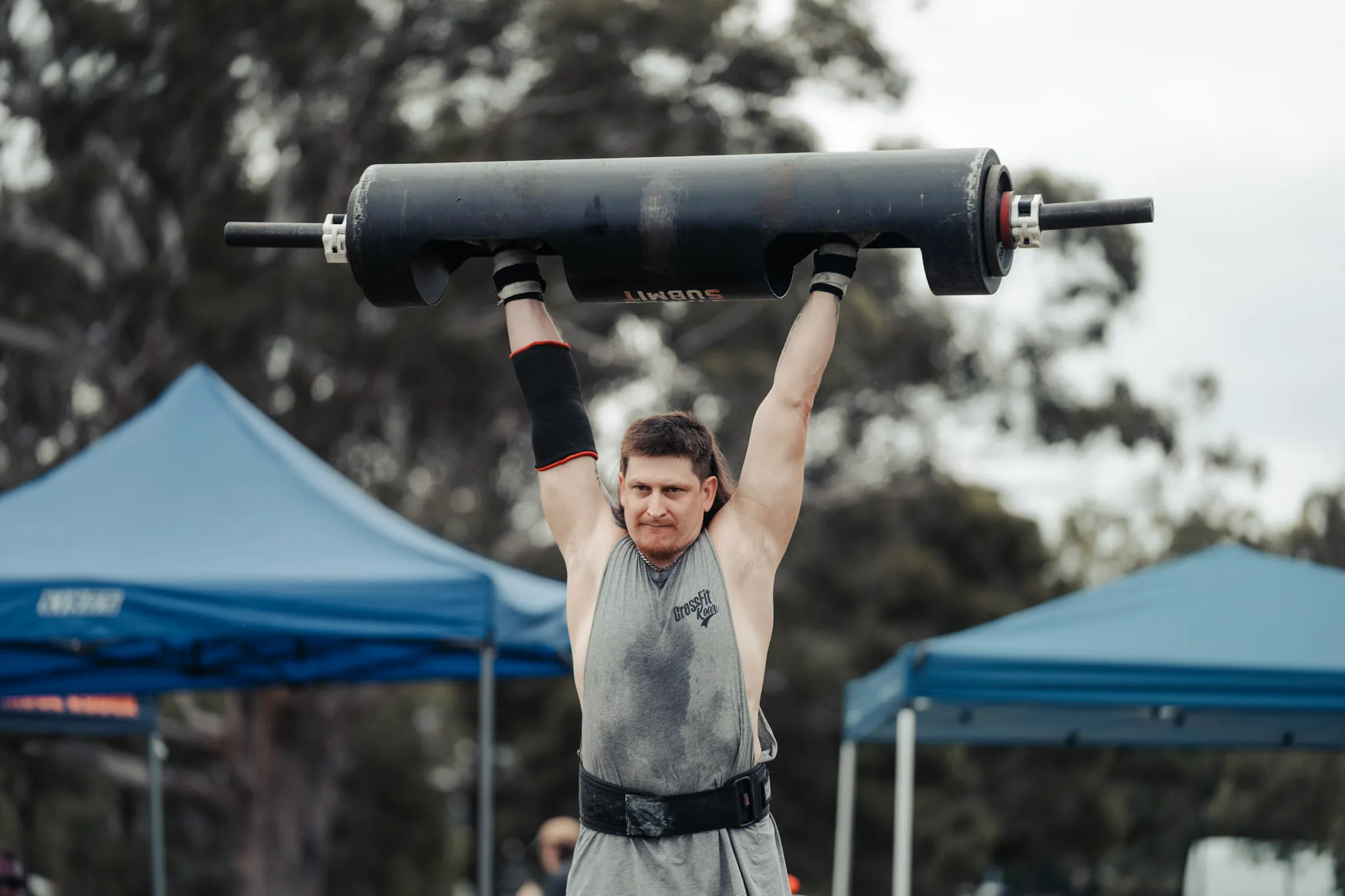 Man wearing grey singlet holding up a barbell. 