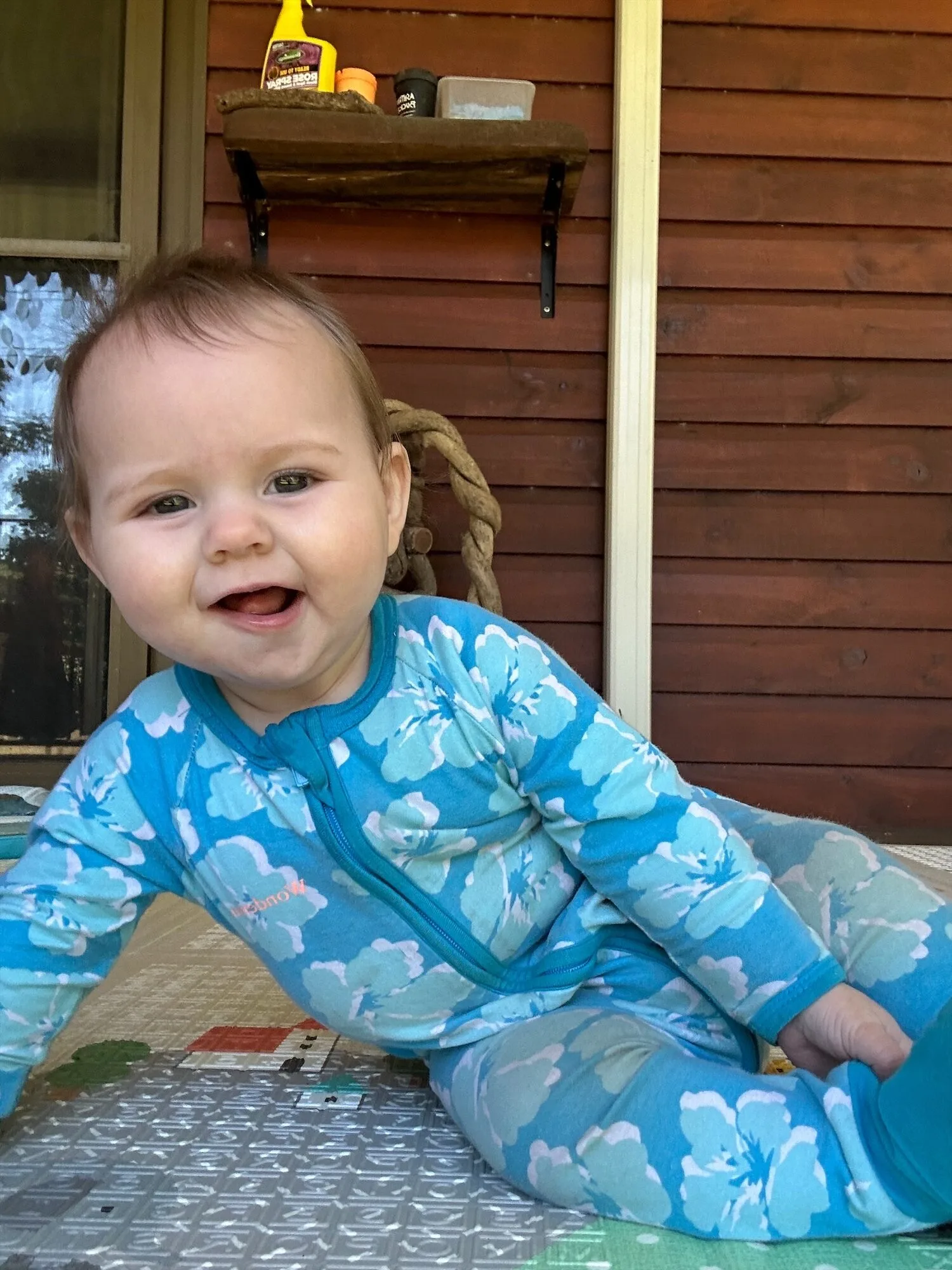 Babay wearing blue overalls smilling at camera.
