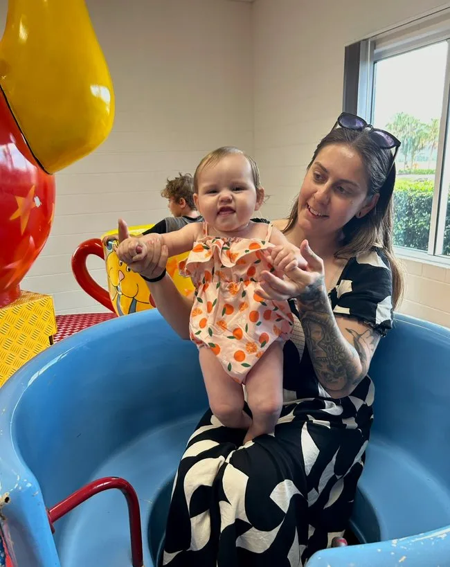 Woman wearing black outfit holding baby and sitting on blue chair. 
