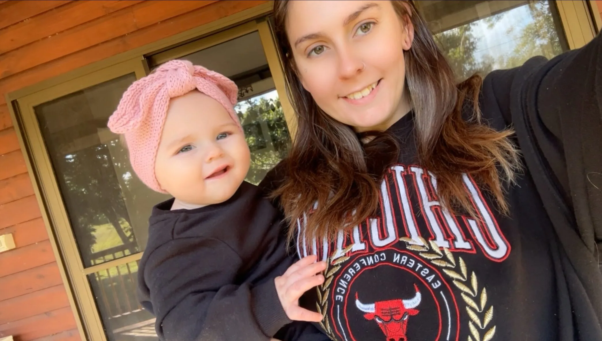 Woman wearing black jumper holding baby with pink headband. 