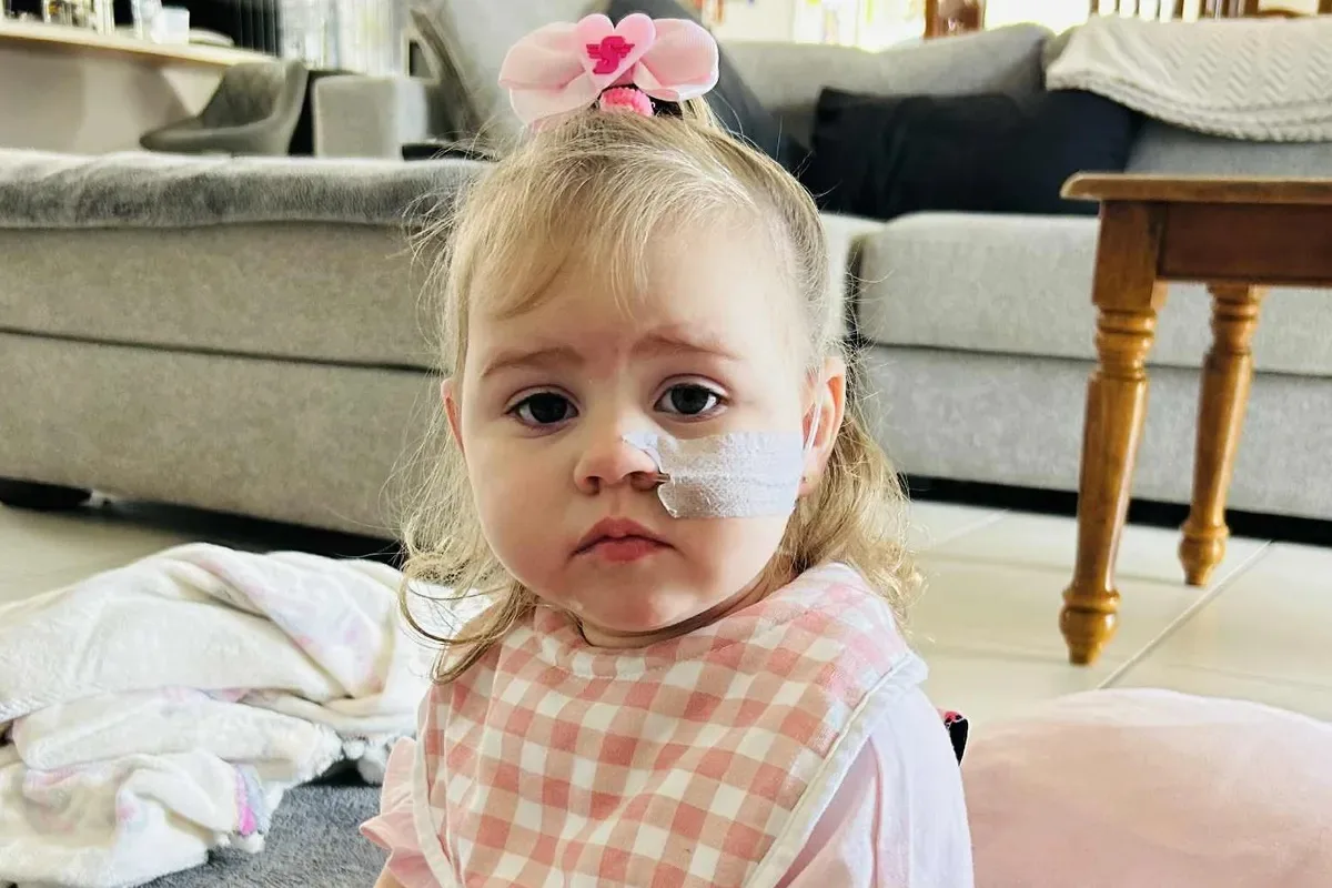 Little girl wearing pink outfit with feeding tube attached to mouth.