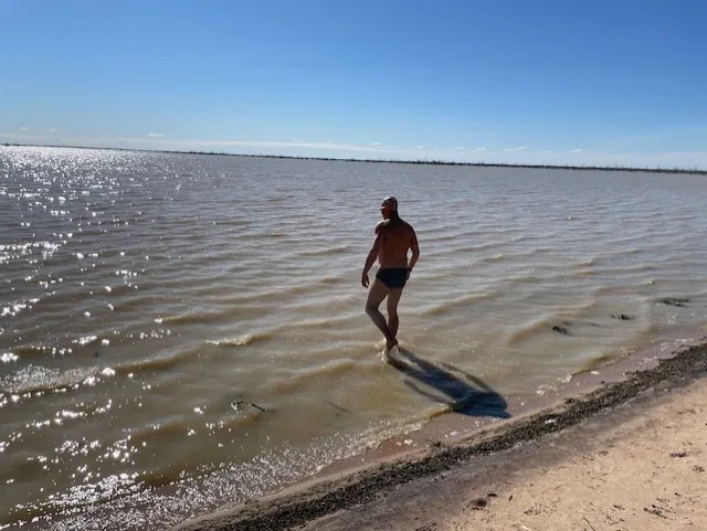 Man walking into a damn in the outback ready to swim.