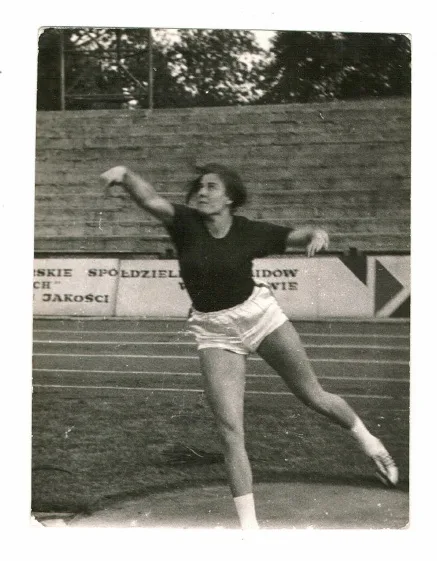 Woman wearing black long sleeve top and white shorts playing shotput on a field. 