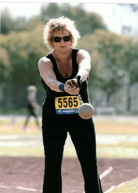 Woman wearing black jumpsuit and sunglasses and practising shotput.