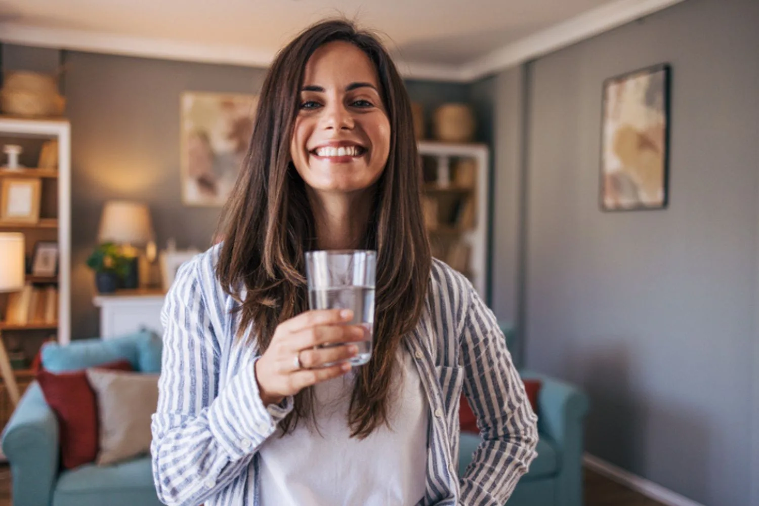 Woman smiling holding glass of water in her living room