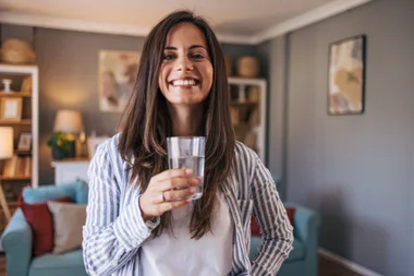 Woman smiling holding glass of water in her living room