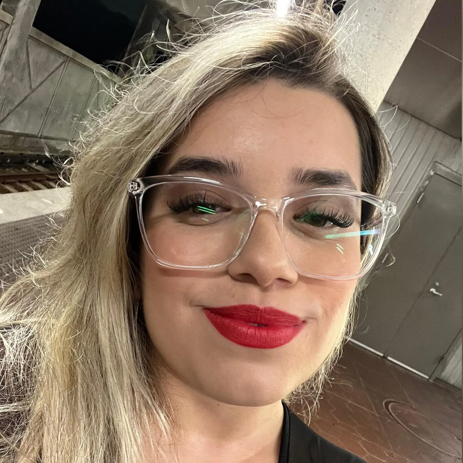 Woman with blonde hair, wearing glasses and red lipstick, smillling at camera.
