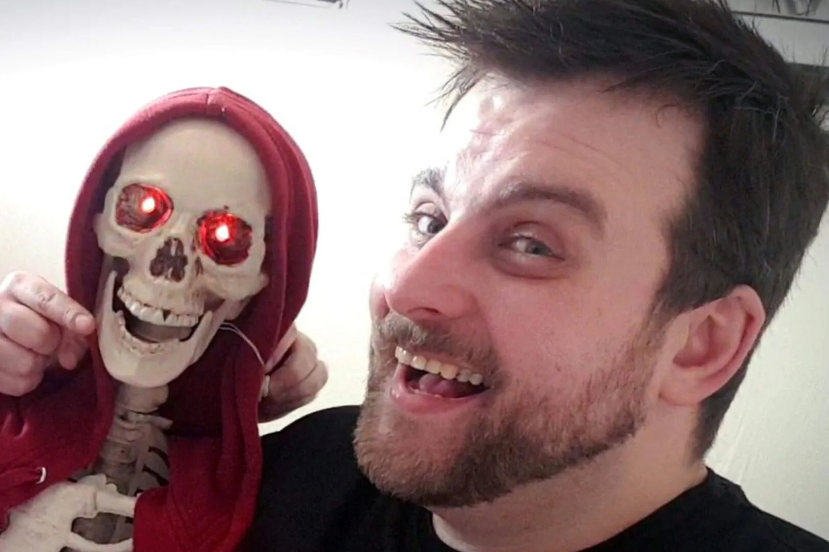Man with short brown smilling holding up a skeleton. 