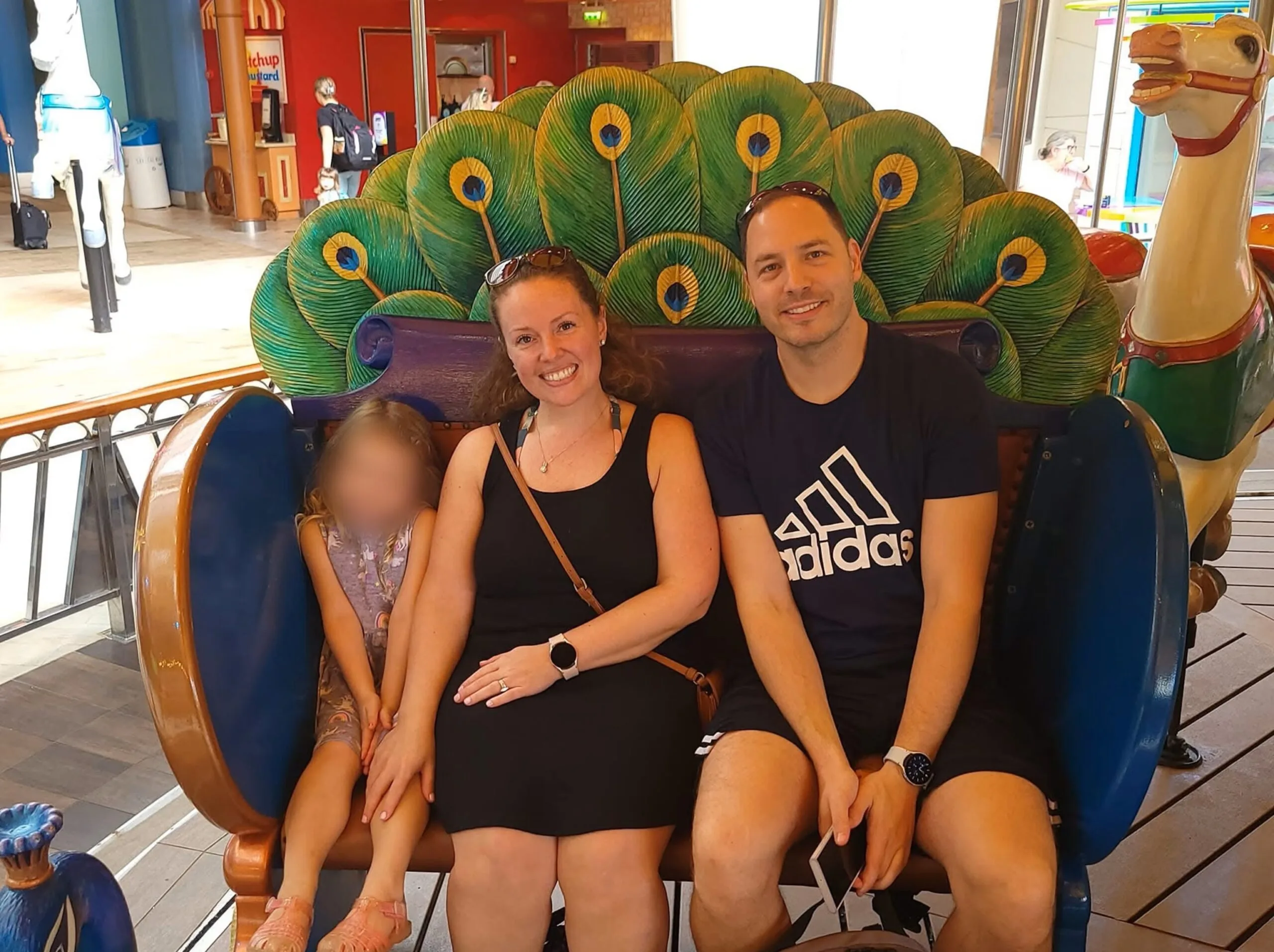 Man wearing black shirt and shorts sitting next to woman wearing black dress, next to a child. All smilling at camera.
