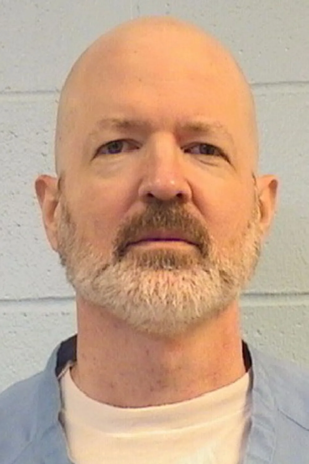 Mugshot of man with whitebeard, wearing prison uniform.