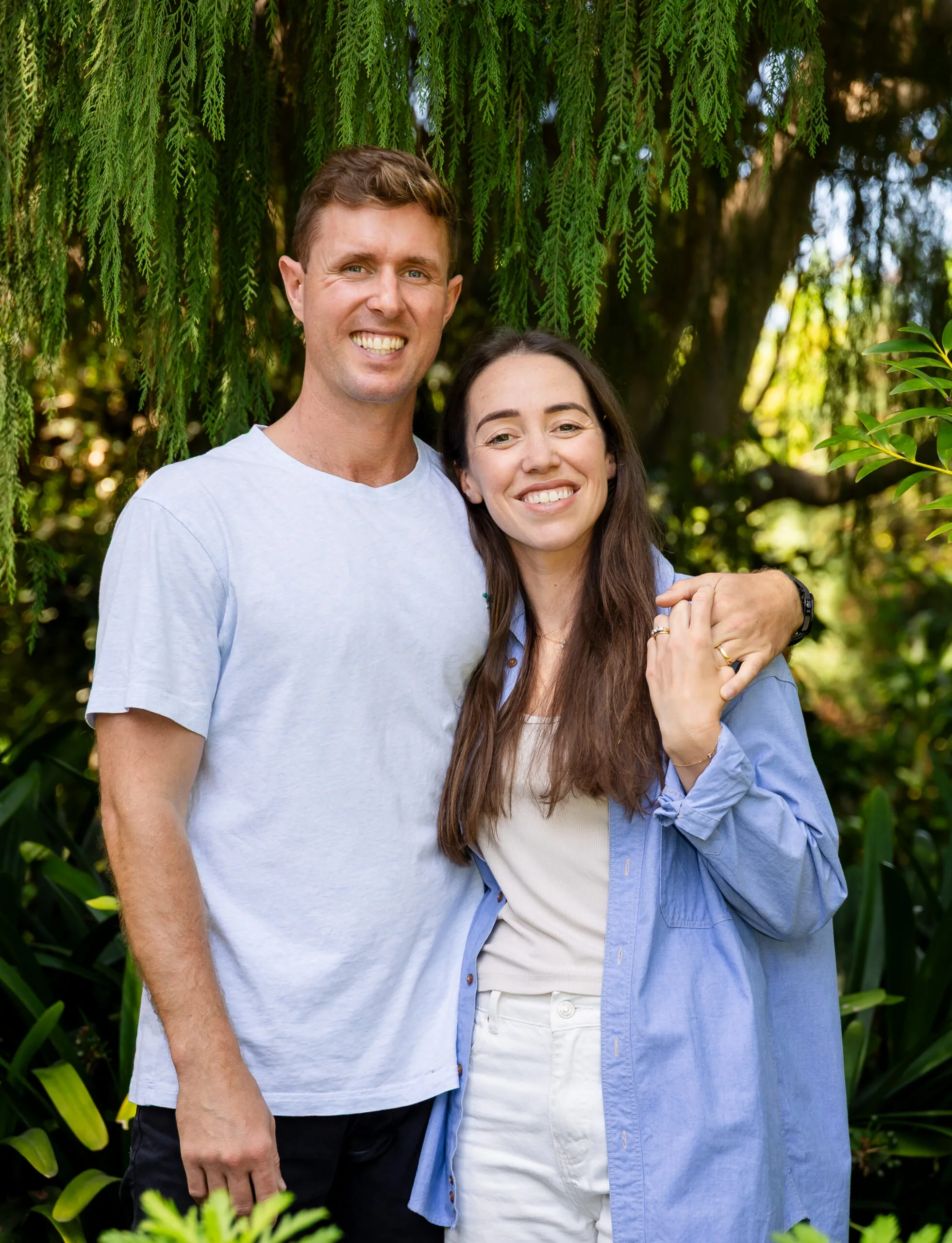 Man wearing blue shirt and smiling wrapping arm around woman with long brown hair, wearing blue shirt as well.