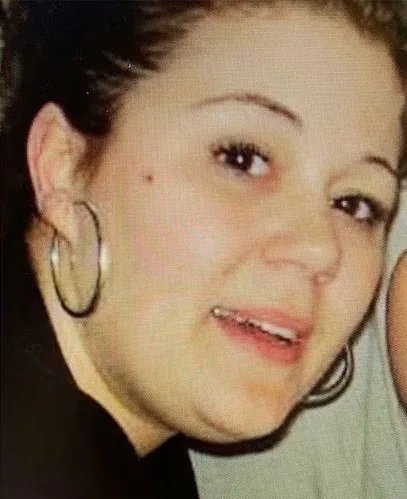 Woman with brown hair in a bun, wearing silver hoops and looking at camera.