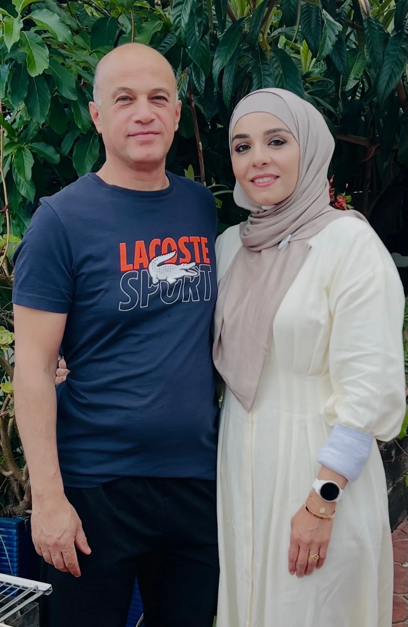 man and woman pose for photo outside she is wearing cream and he is wearing navy tshirt dark pants
