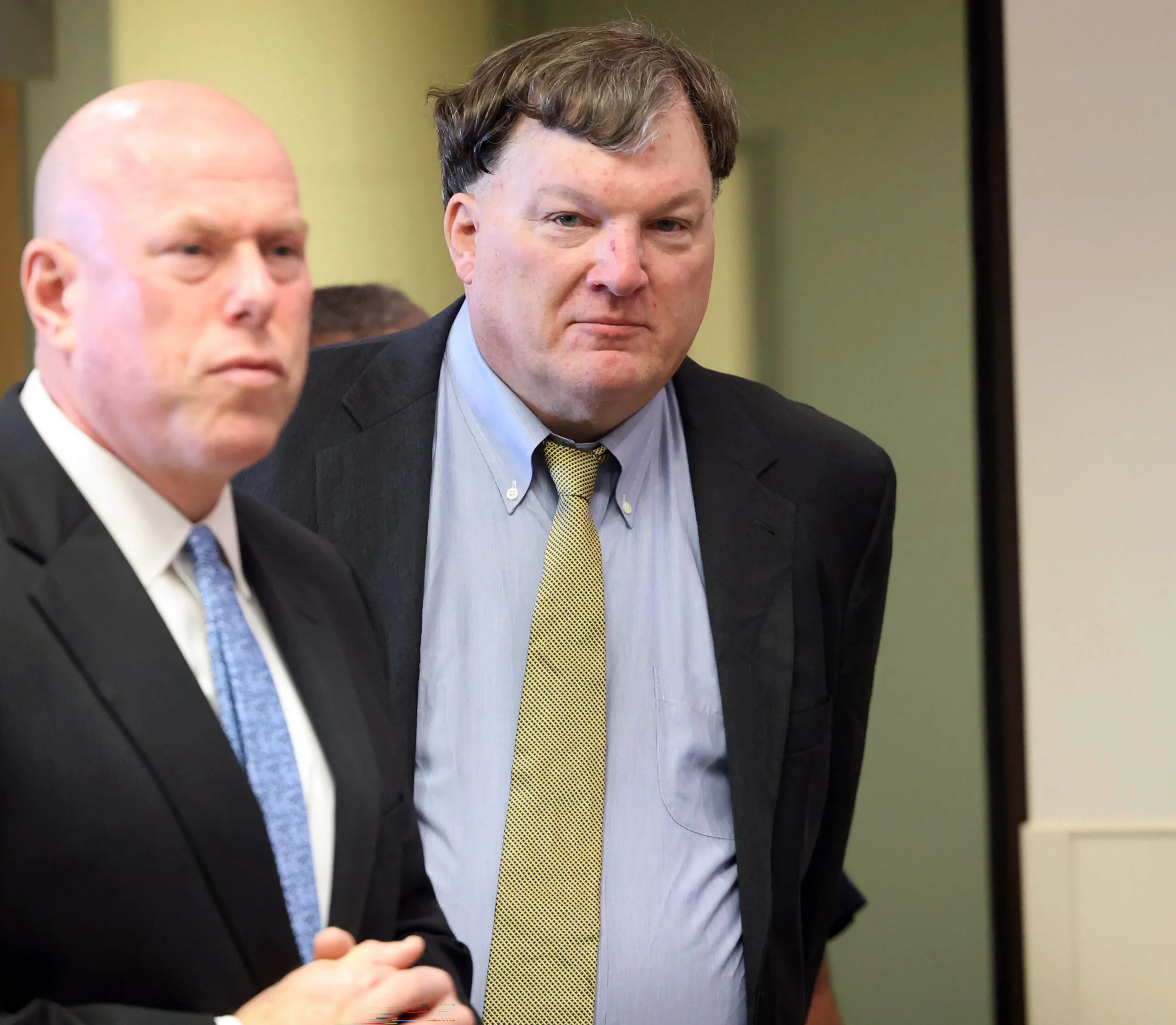 Man in a suit looking at camera while being escorted by another man.