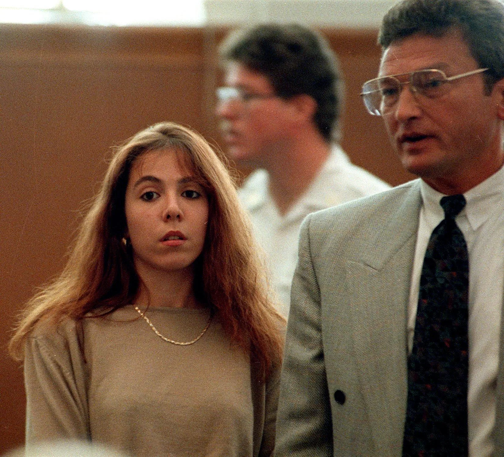 Woman with long brunette hair, wearing green top next to man in a suit in a court room.
