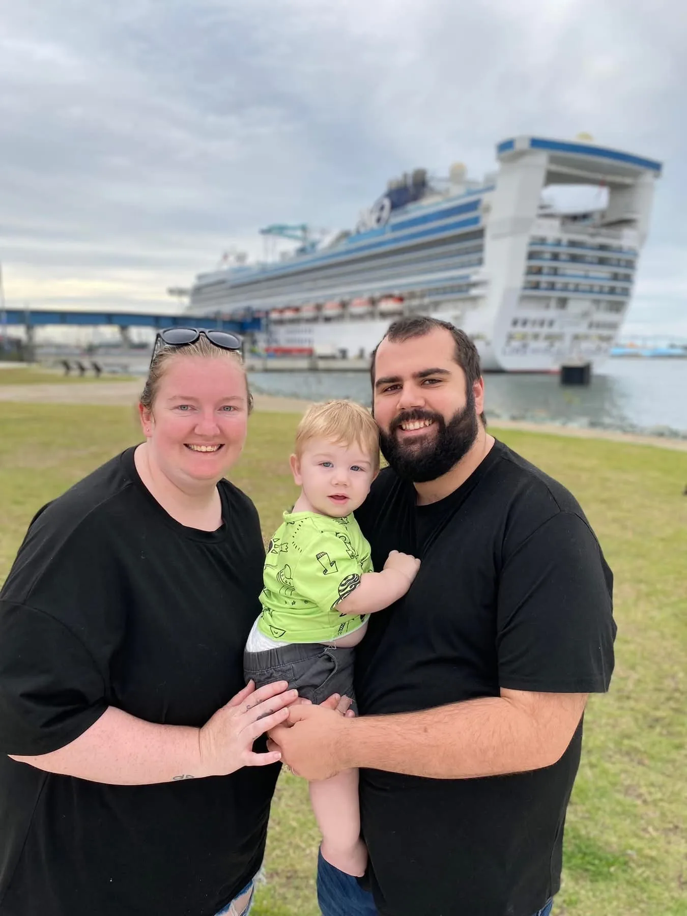 Woman wearing black shirt holding boy toddler with man wearing black shirt. All smiling at camera.