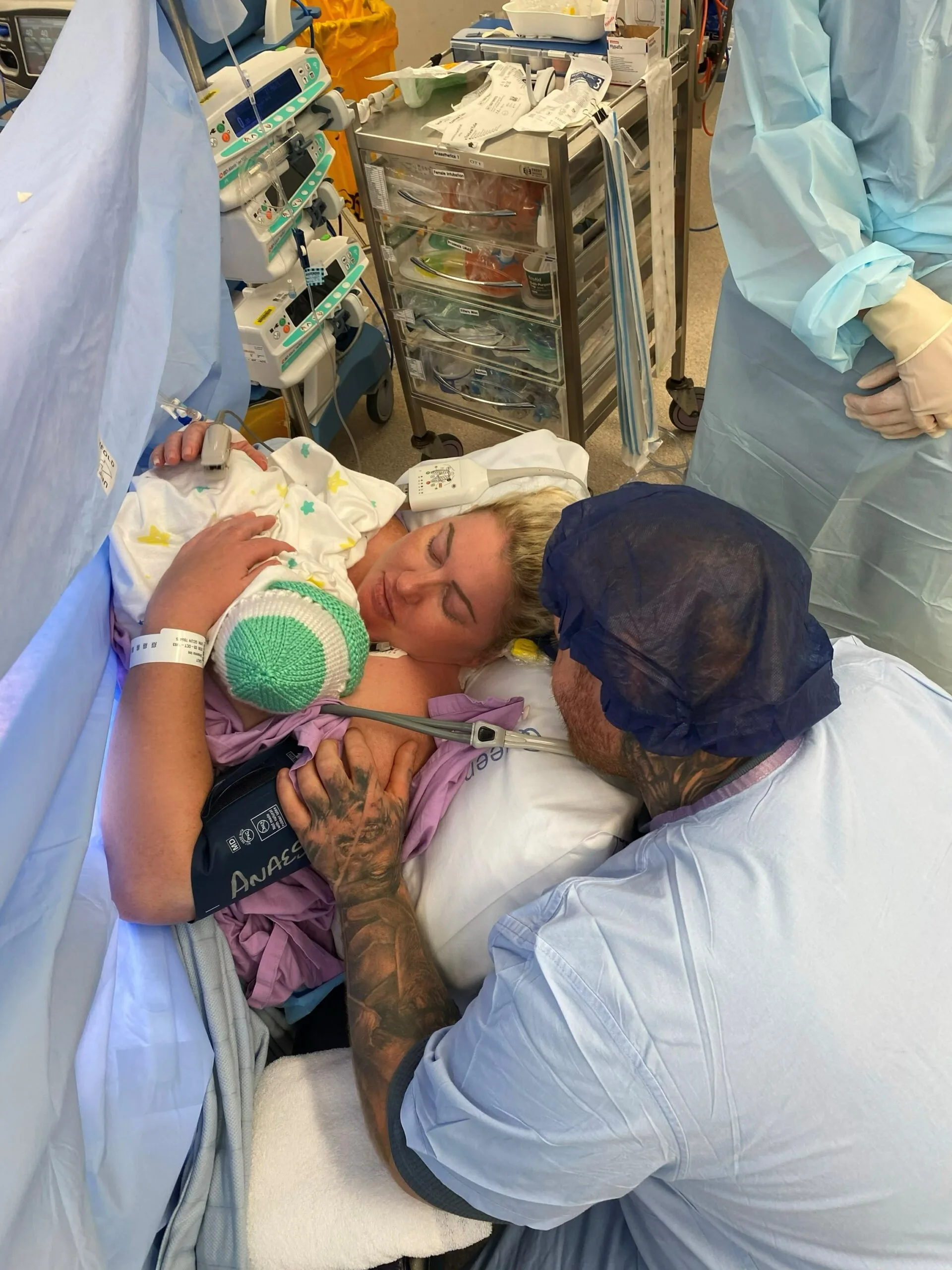 woman on hospital bed with newborn baby on chest, with man next to her looking over.