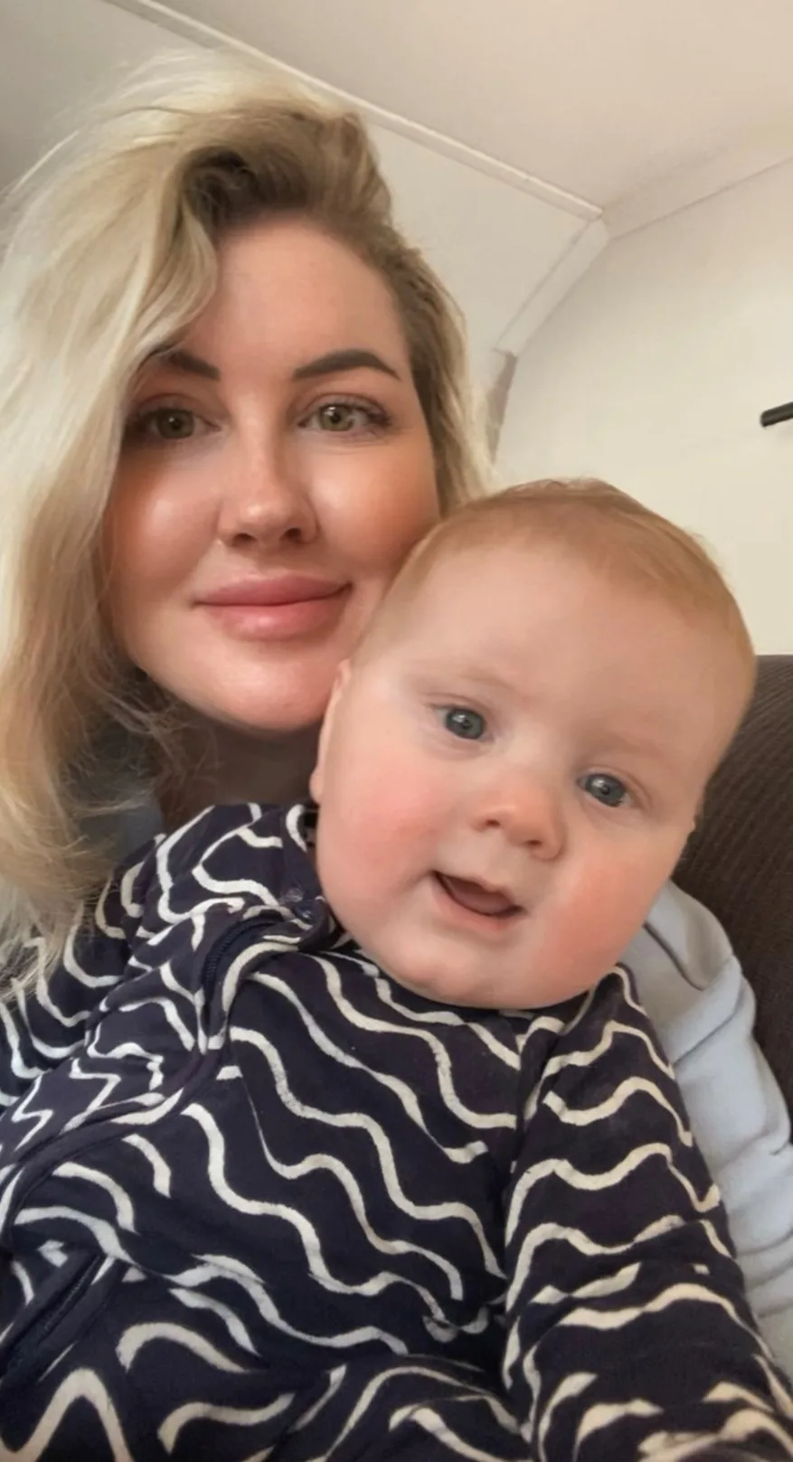 woman with blonde hair, holding newborn baby and both smiling at camera.