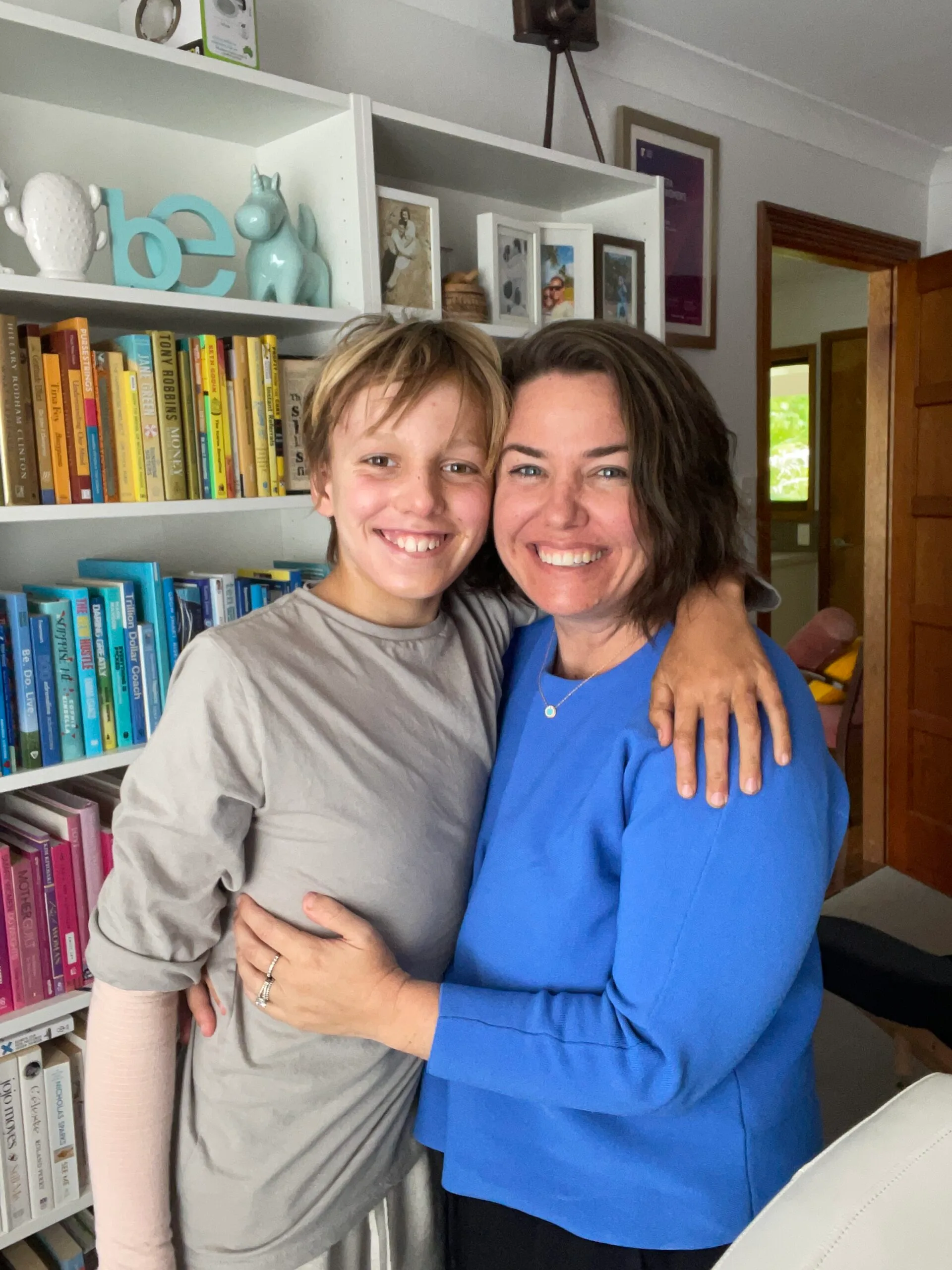 Young boy wrapping arms around woman wearing blue shirt and both smiling at camera.