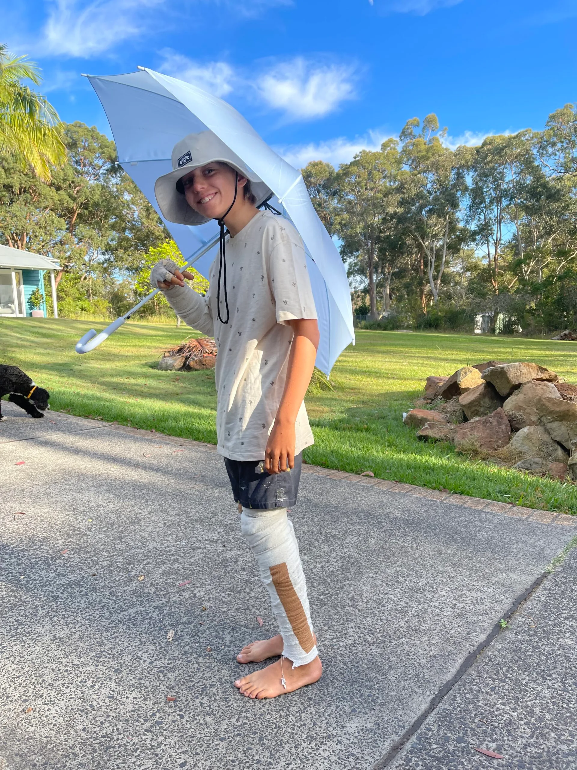 Young boy wearing shirt and shorts, holding up an umbrella in the sun.