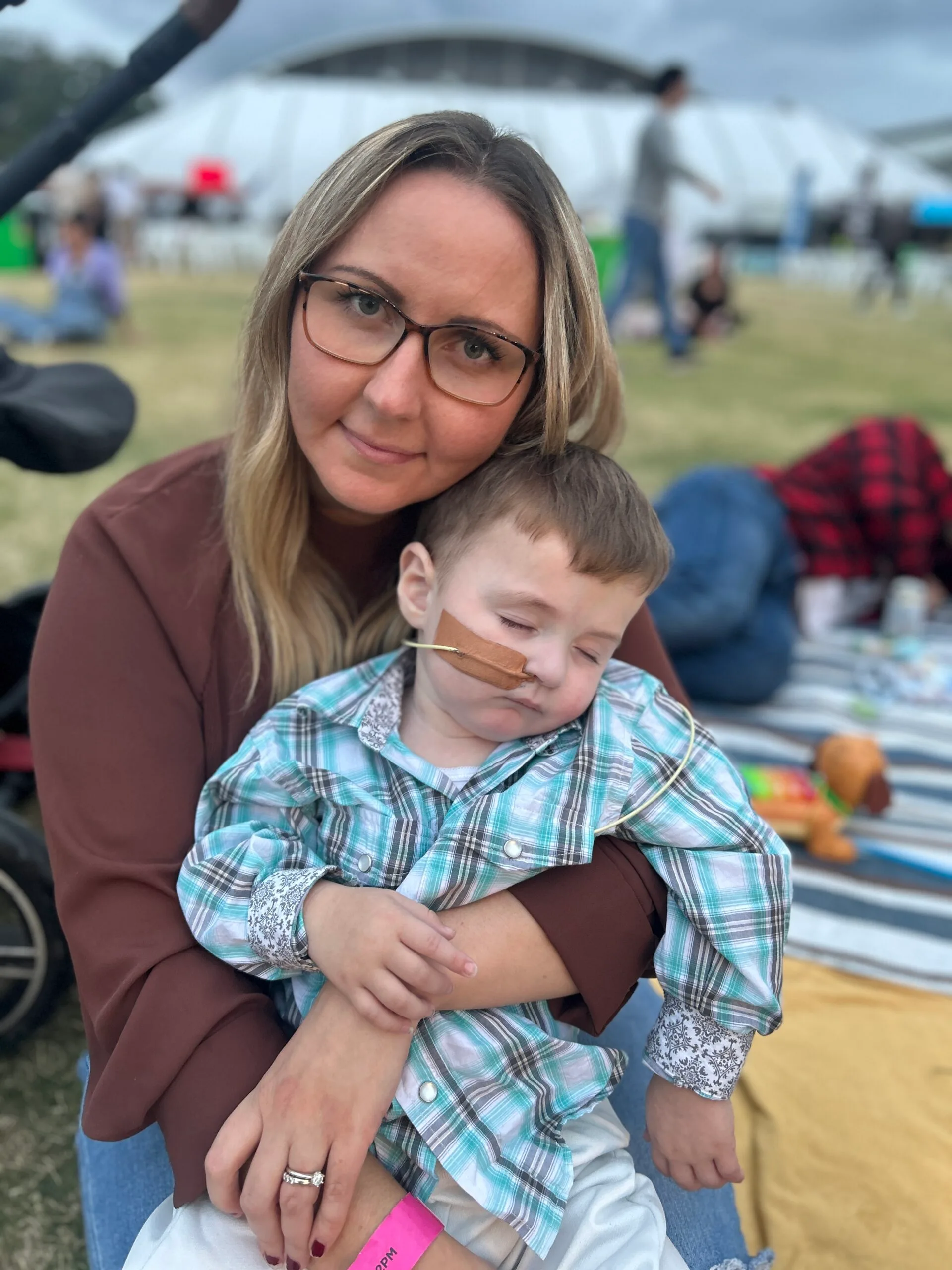Woman with blonde hair, wearing glasses, carrying sleeping toddler. 