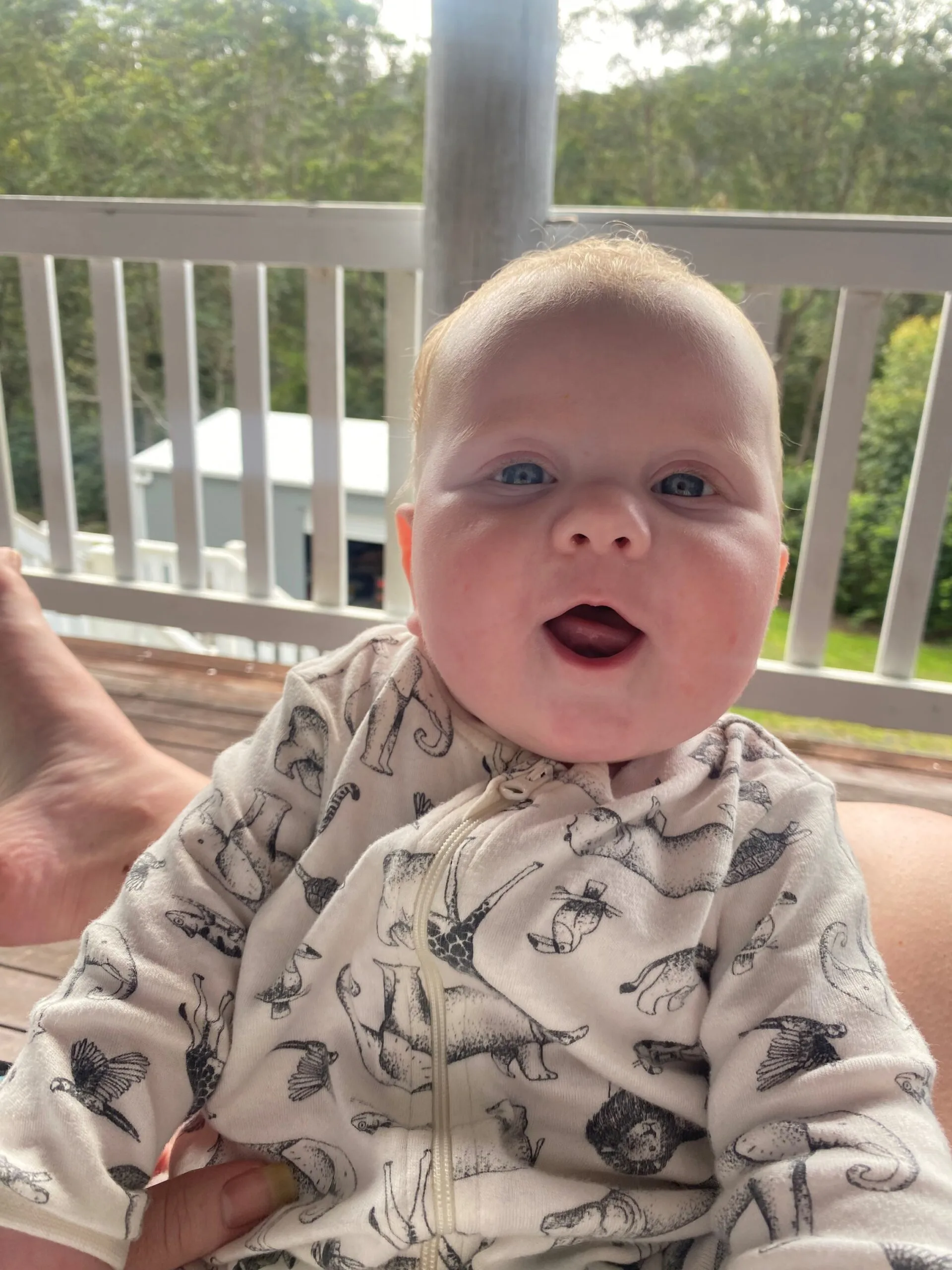 Newborn baby wearing jumpsuit and smiling at camera.