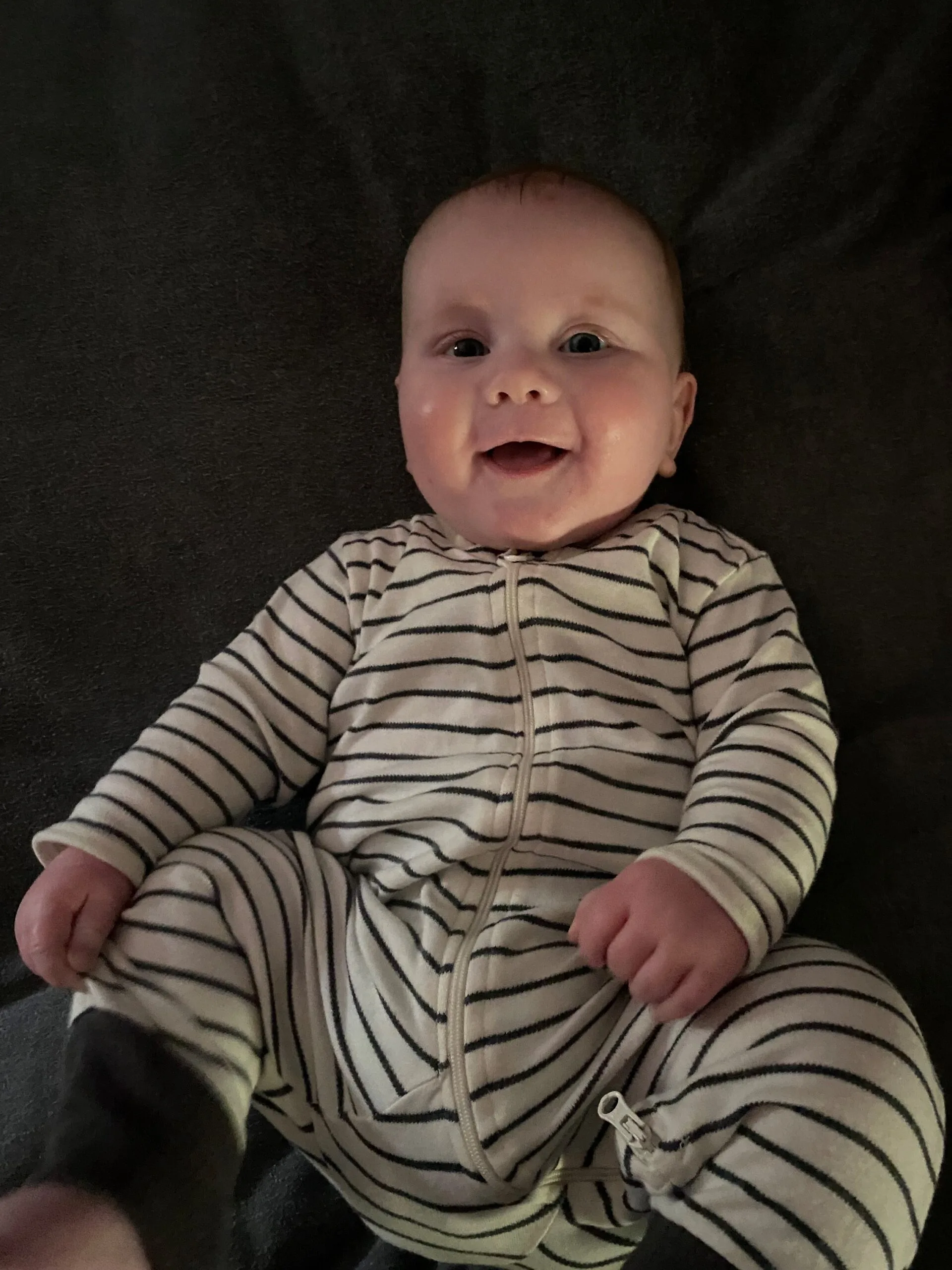 Newborn baby wearing stripped jumpsuit and smiling at camera.