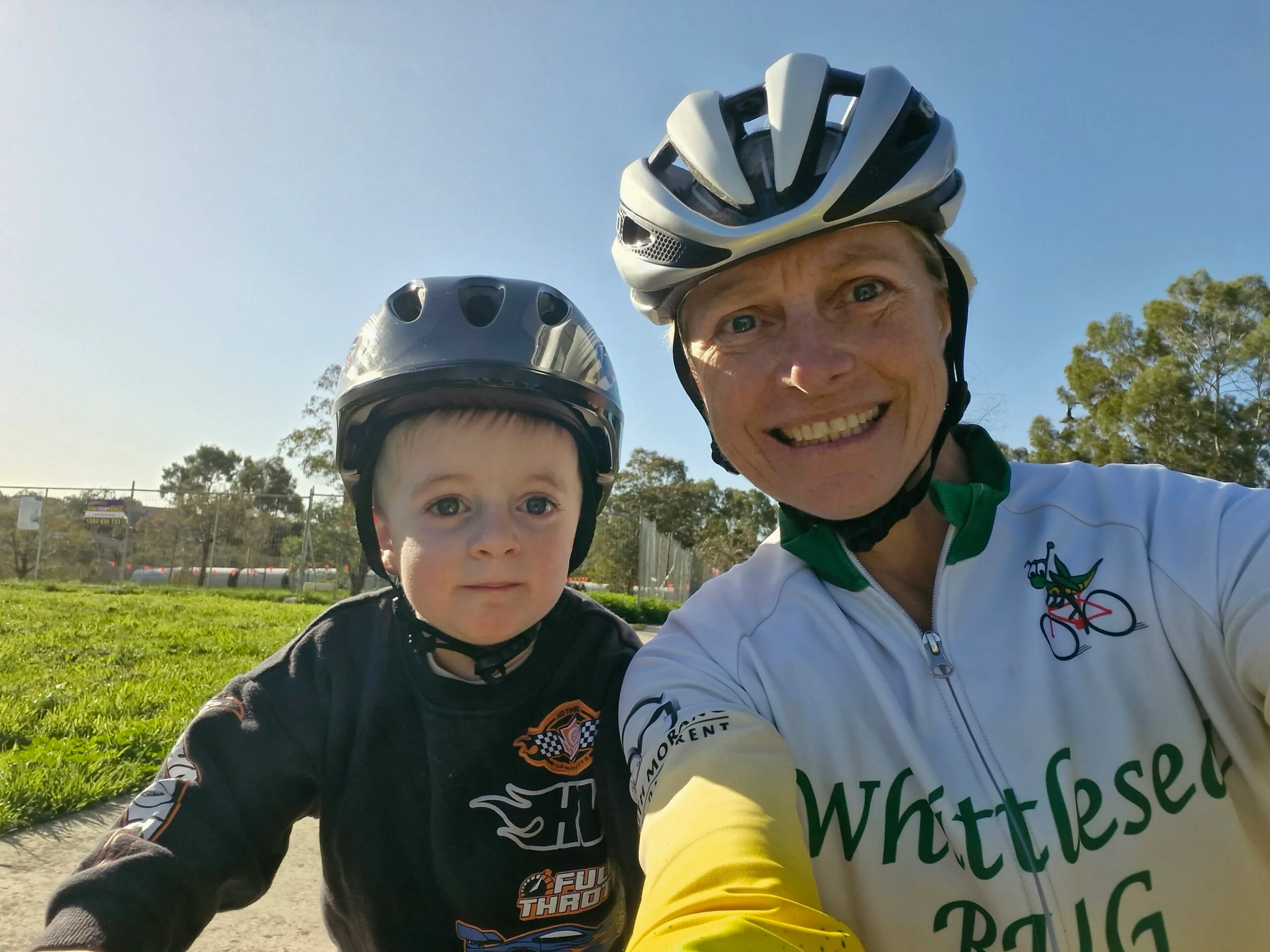 Woman and toddler both wearing helmets and smiling at camera. 