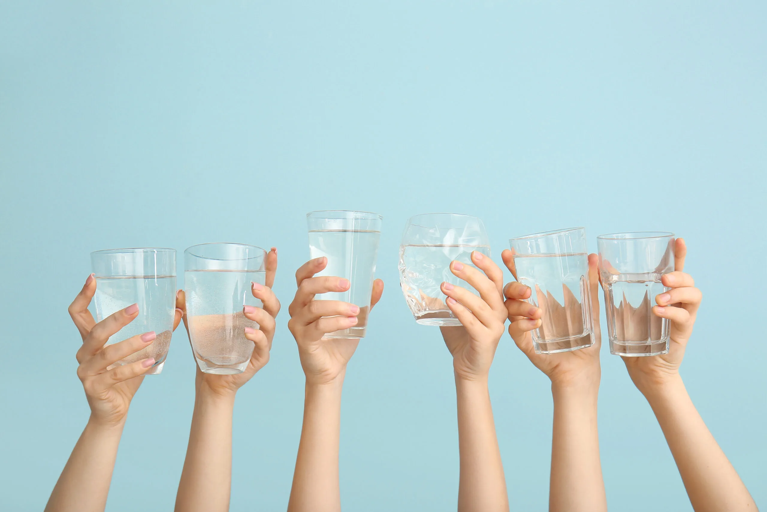 Several hands holding up glasses of water.