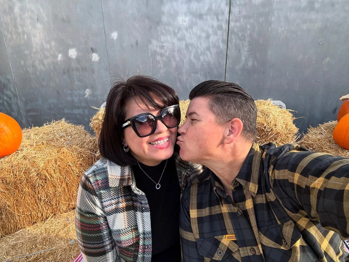 Woman with short black hair smiling at camera with another woman kissing her cheek.