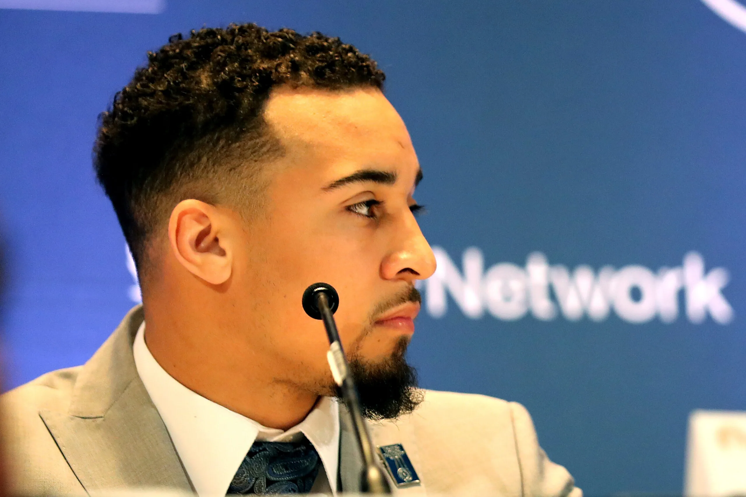 Sportsman wearing suit and sitting infront of mic staring into direction.