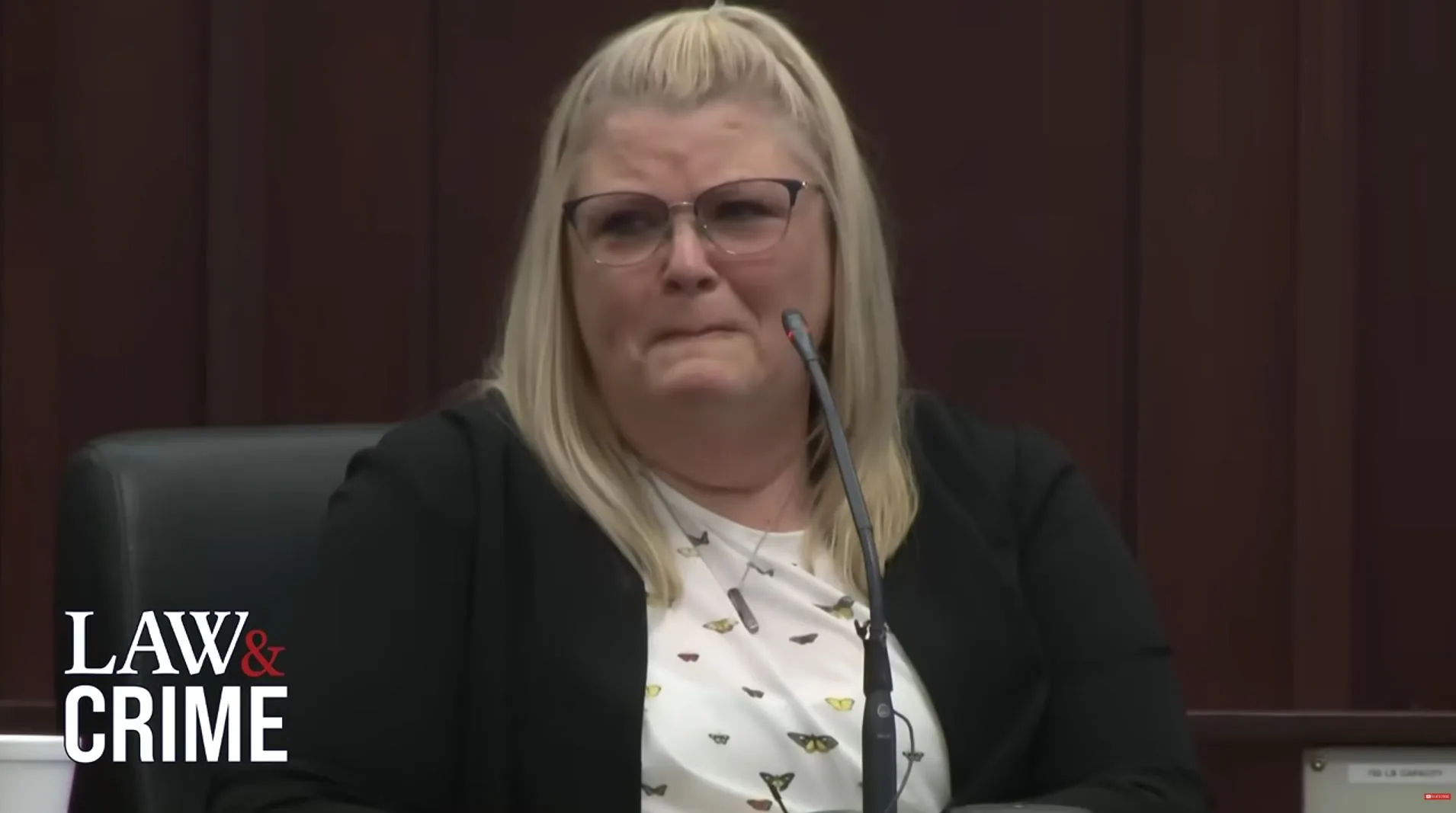 Woman with blonde hair, wearing glasses and looking emotional during interview.