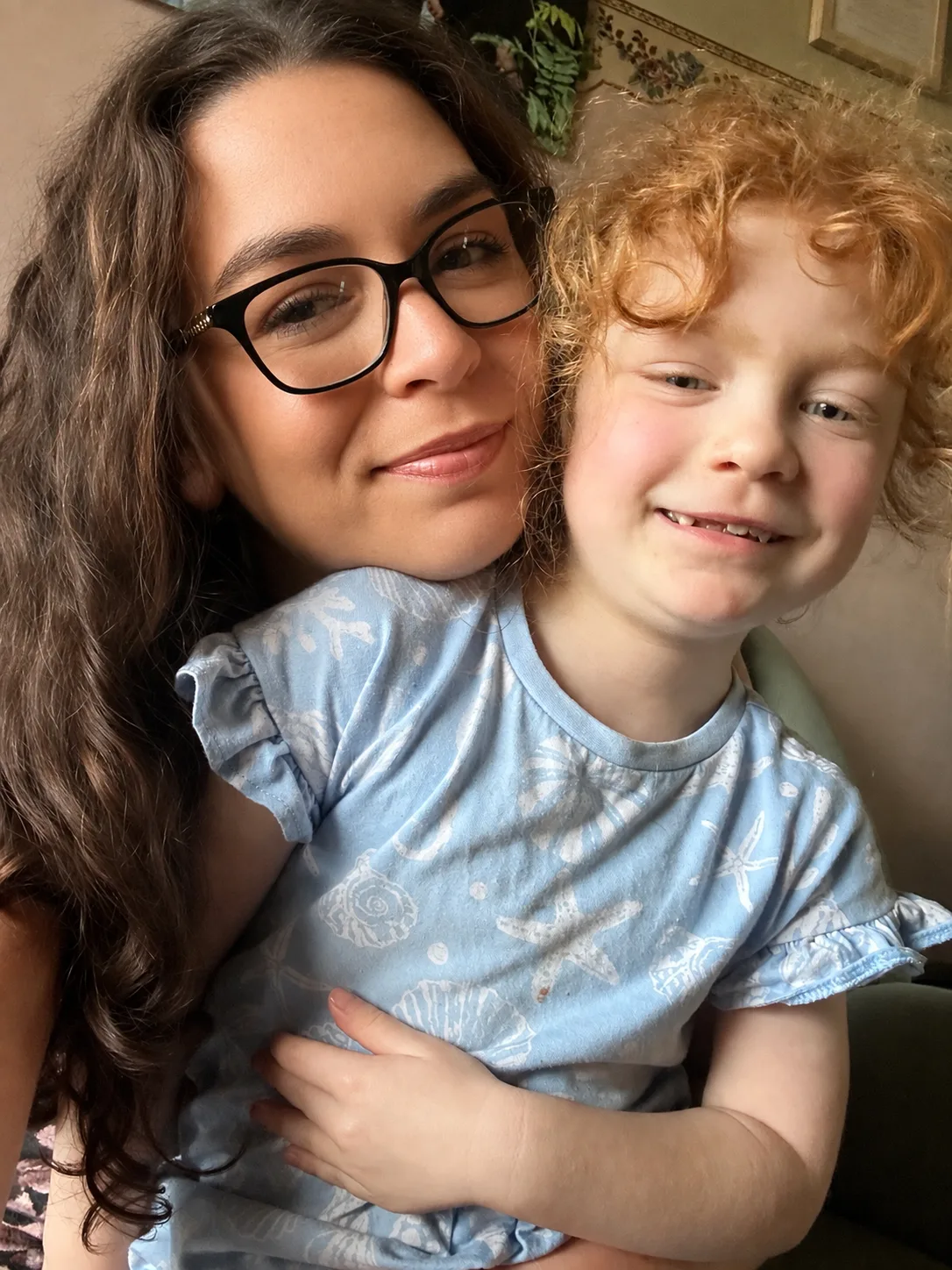 Woman wearing glasses, holding little girl with strawberry blonde hair. Both smiling at camera