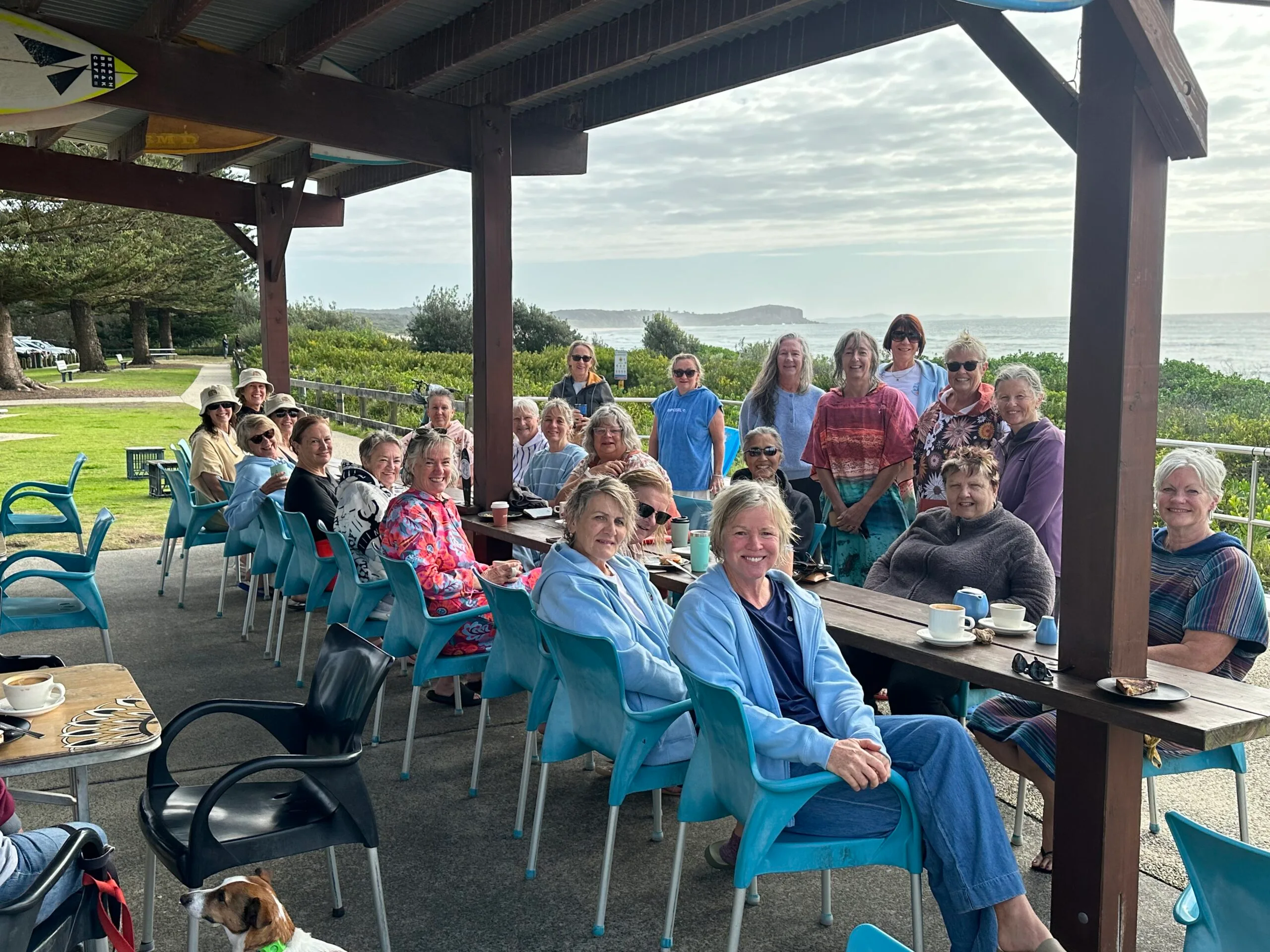 Large group of women sitting around table and smiling at camera.
