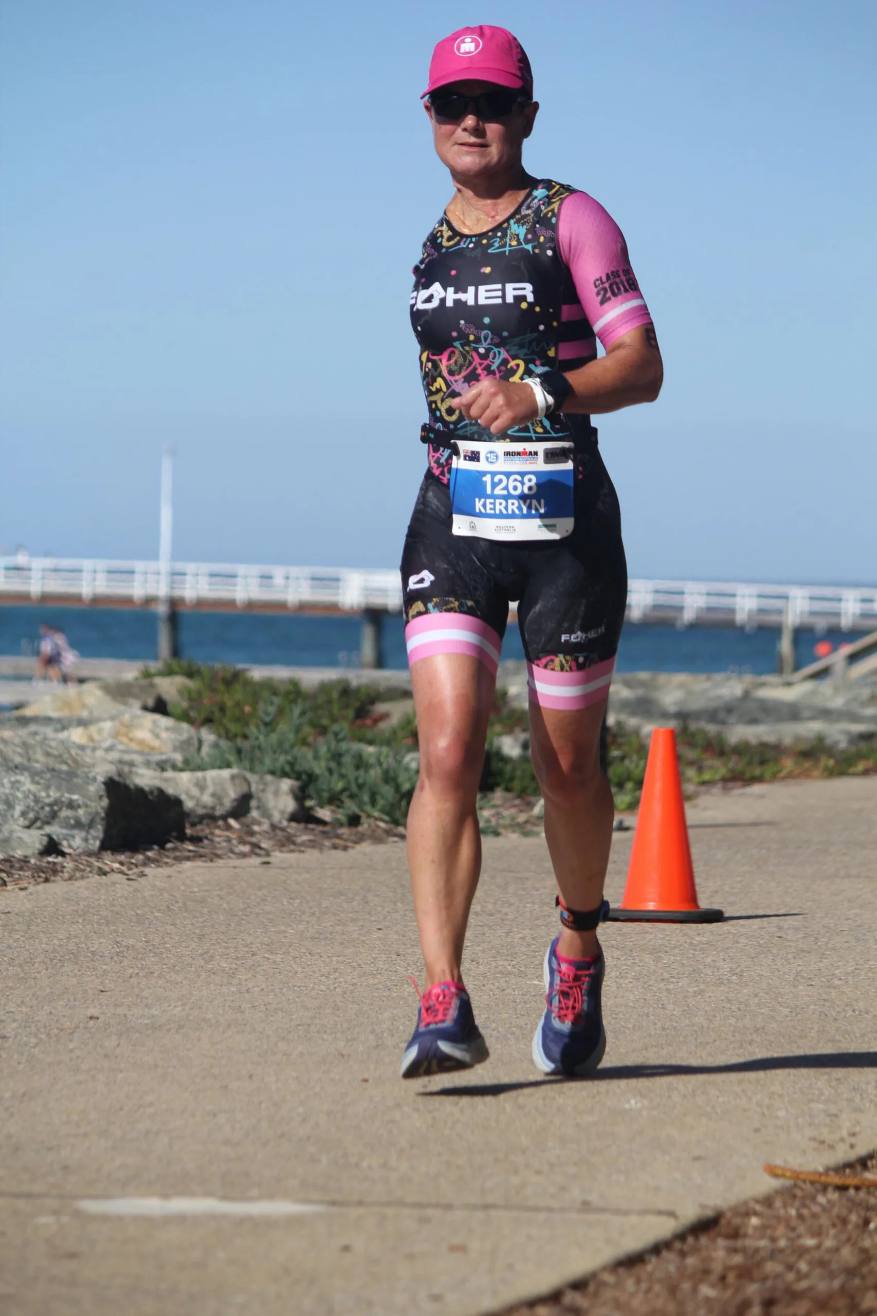Woman with one arm, wearing sunglasses, hat, running gear and running down a track.