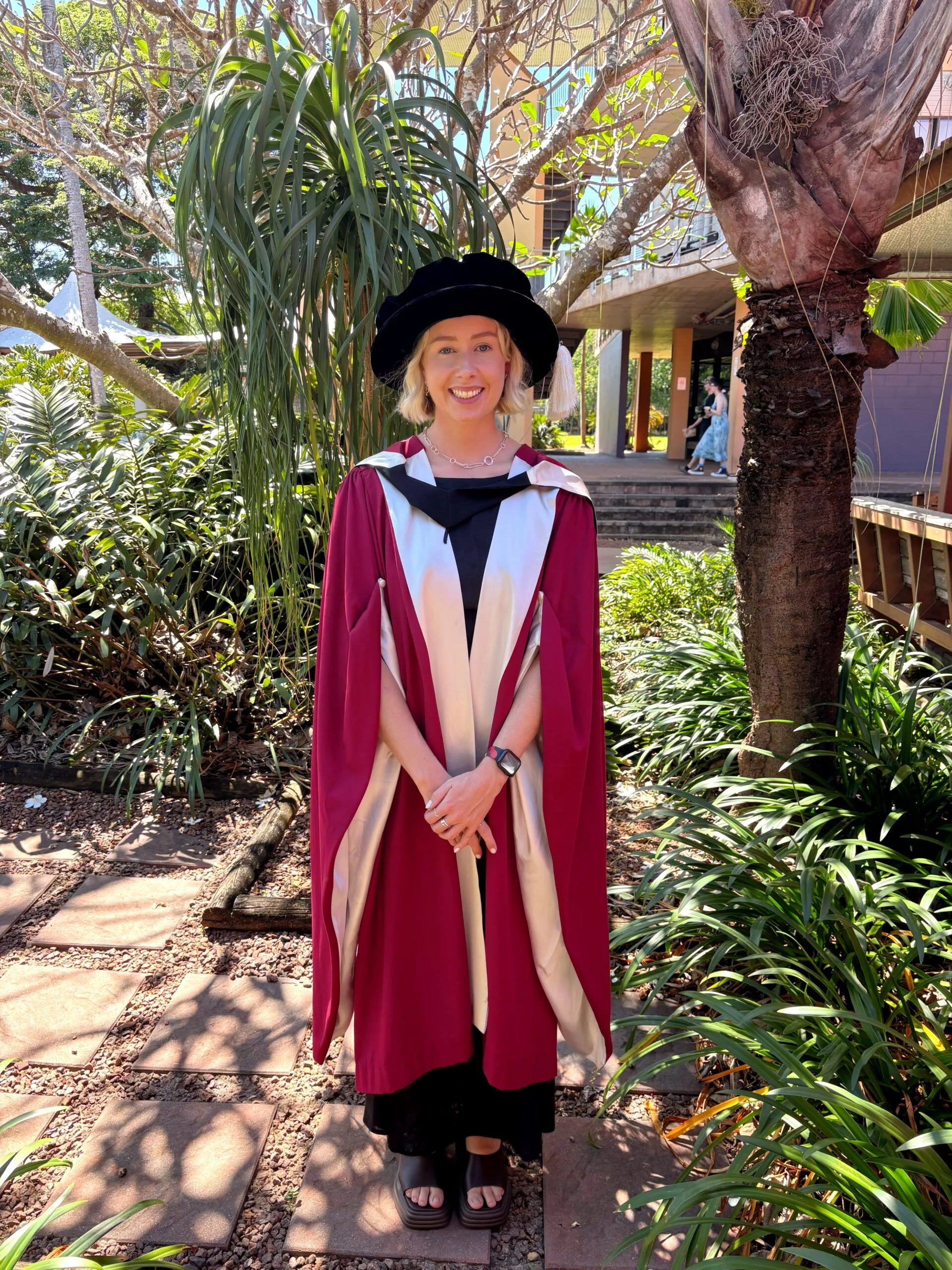Woman with short blonde hair wearing red graduation cape and smiling at camera.