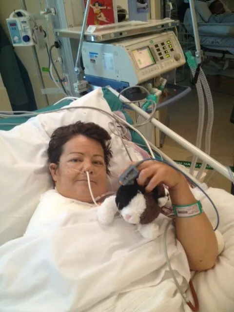 Woman in hospital hooked up to machines, smiling at camera.