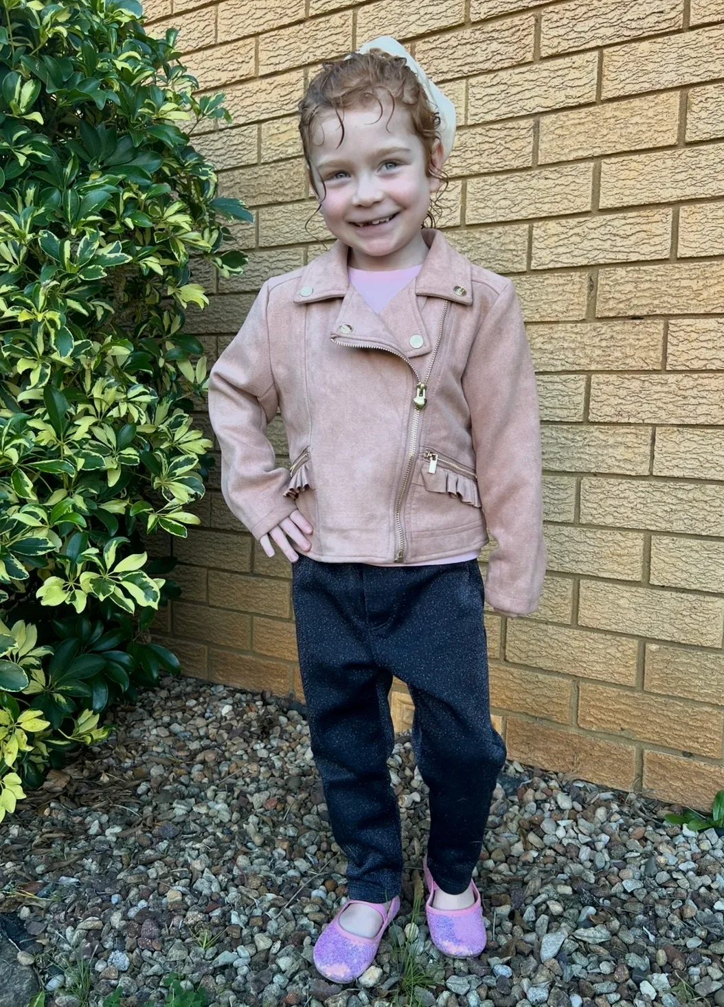 Little girl with strawberry blonde hair, wearing jacket and smiling at camera.