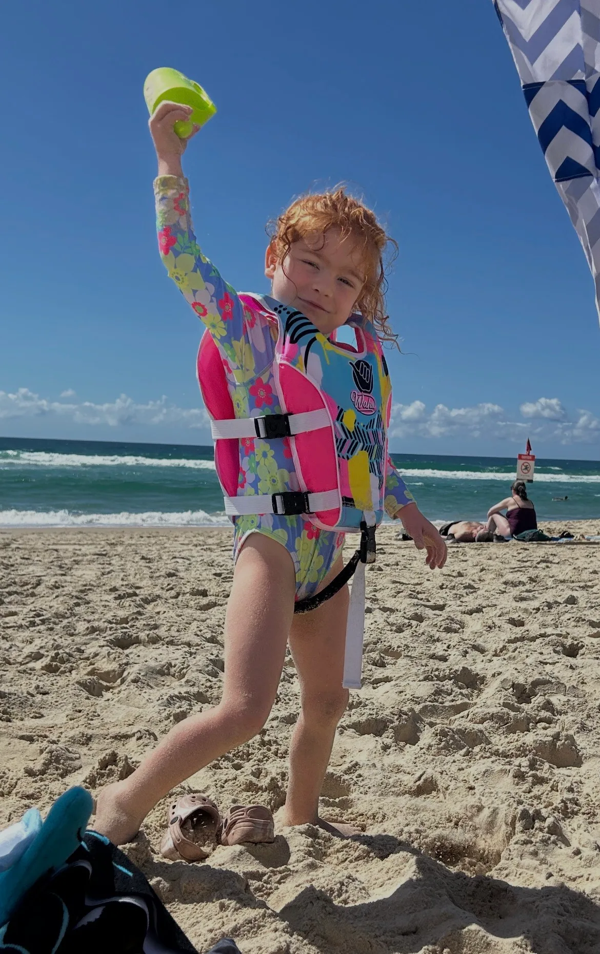 Little girl wearing swimsuit at the beach and holding up a toy.