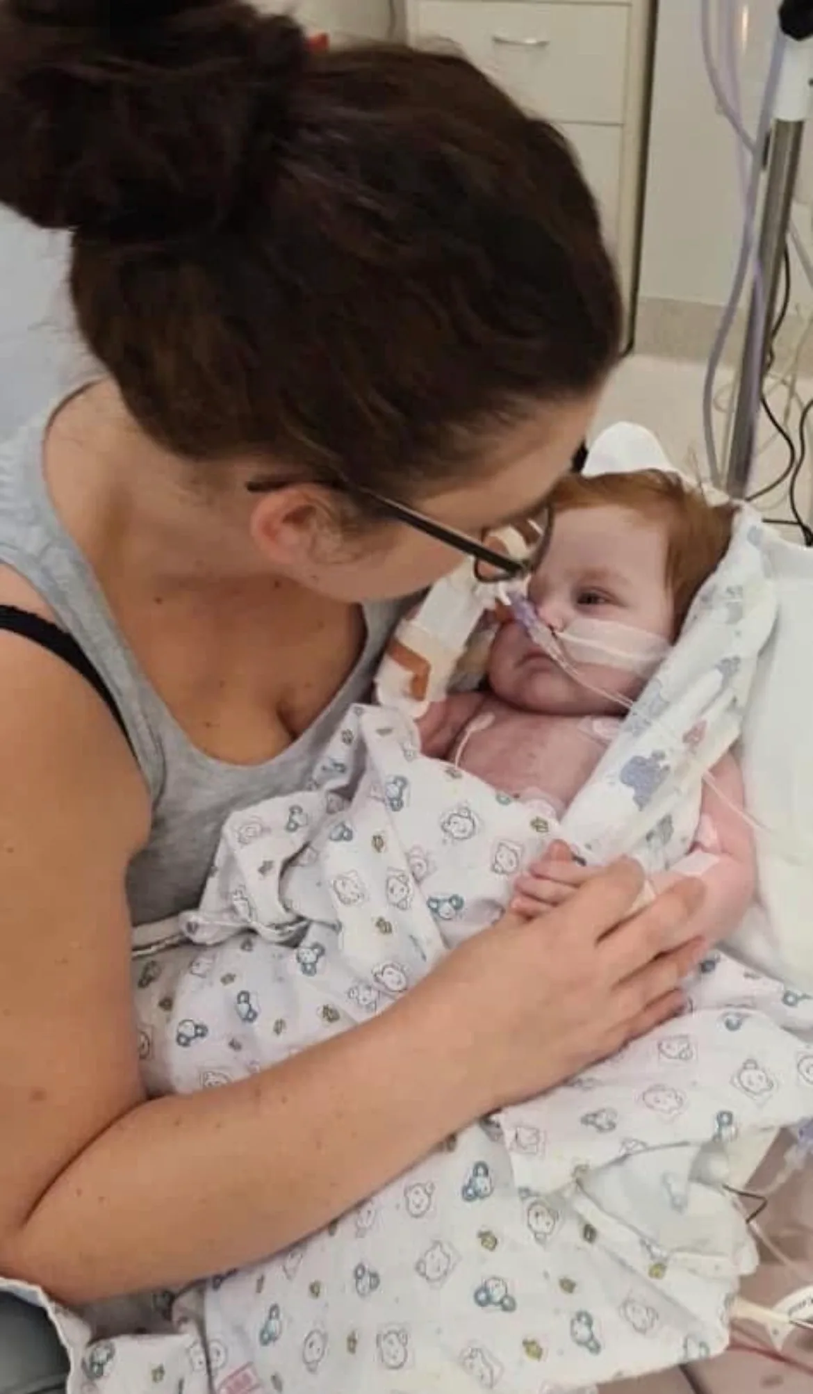 Woman holding new born baby with feeding tube in hospital.